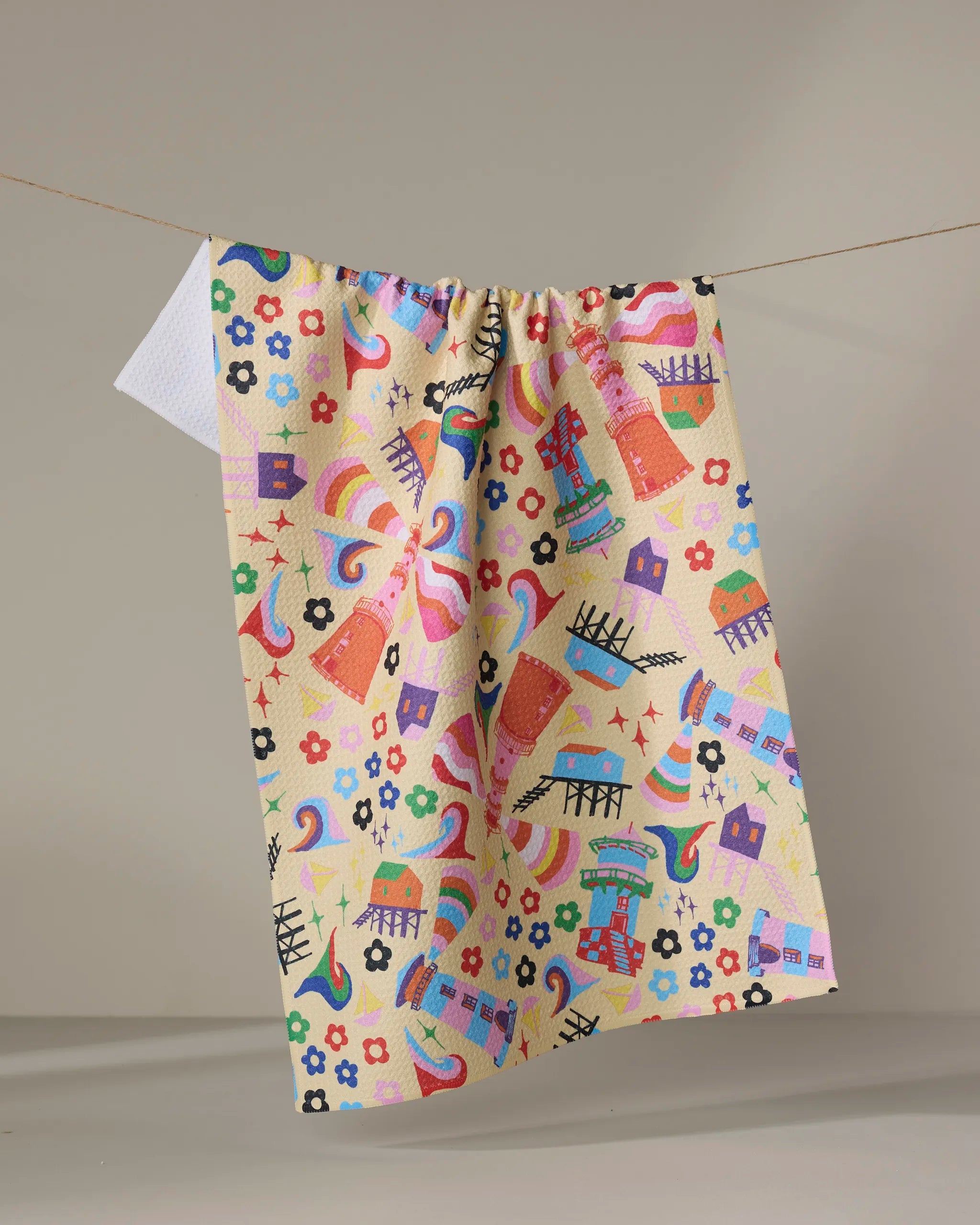 The Ania Zwara Art "My Place" dish towel, featuring playful abstract patterns—rainbows, hearts, shapes, and flowers—hangs on a clothesline against a plain backdrop.