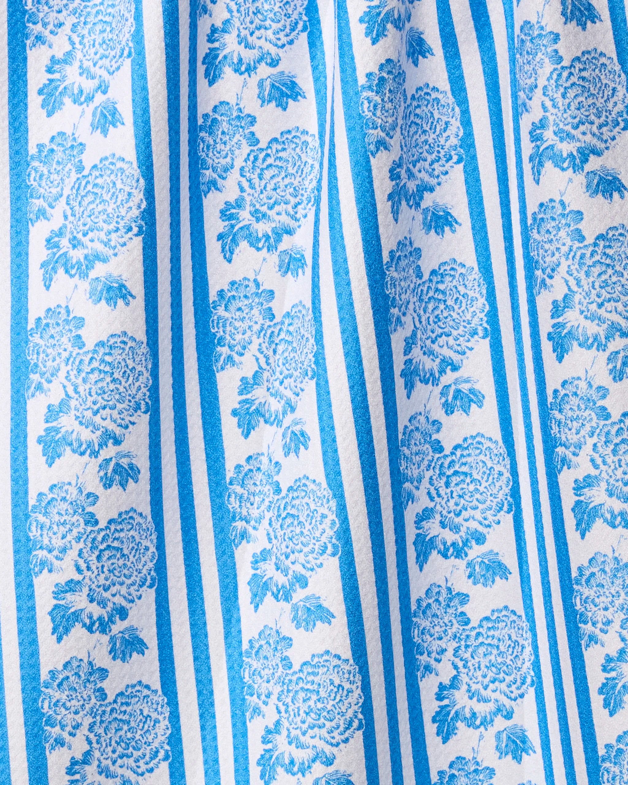 The Geometry Mykonos tea towel features blue floral patterns and vertical stripes on white textured fabric. Ultra-absorbent and stylish, it brings vintage charm to your kitchen.