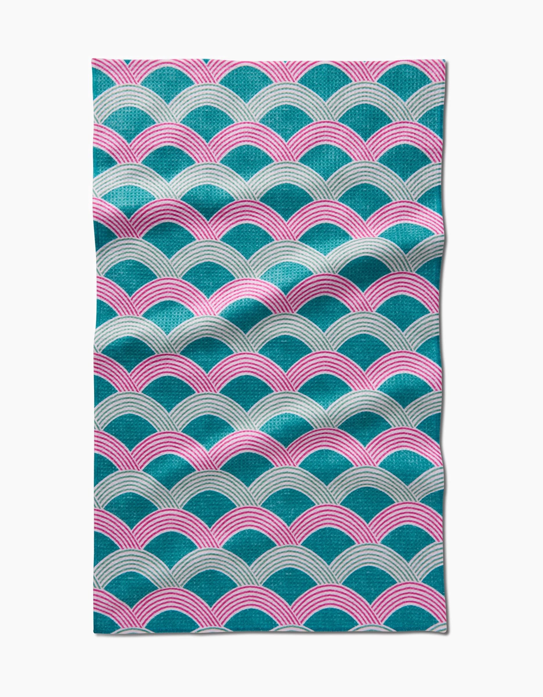 The Nalin tea towel by Amy MacCready features a repeating pattern of teal, pink, and white overlapping arches on Geoweave fabric made from recycled materials, shown with slight wrinkles against a white backdrop.