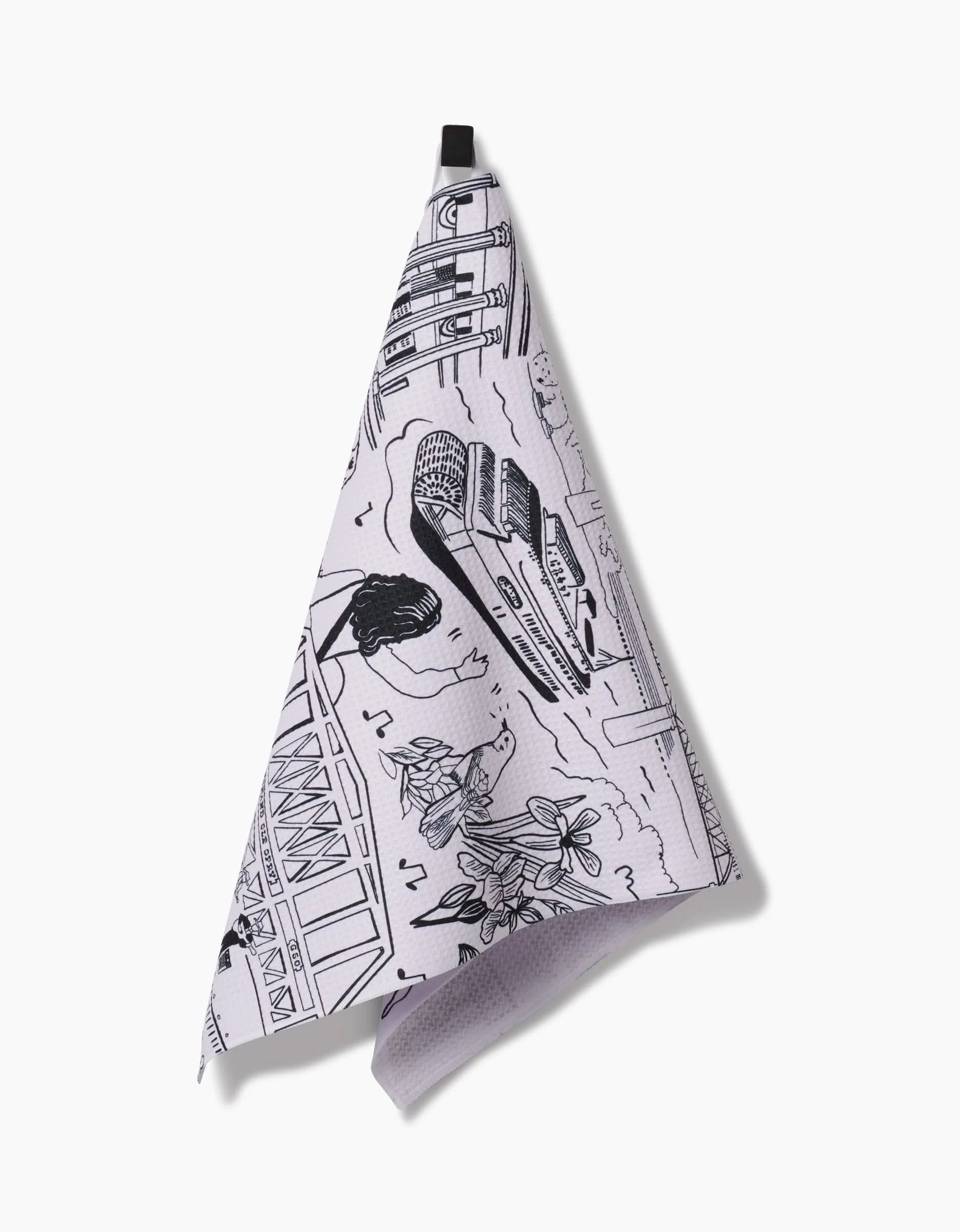 The Nashville Tea Towel by Elisabeth Wing is white, made from recycled materials, and features black line drawings of a bridge, classic car, plants, and musical notes. It hangs by a black loop against a plain white background.