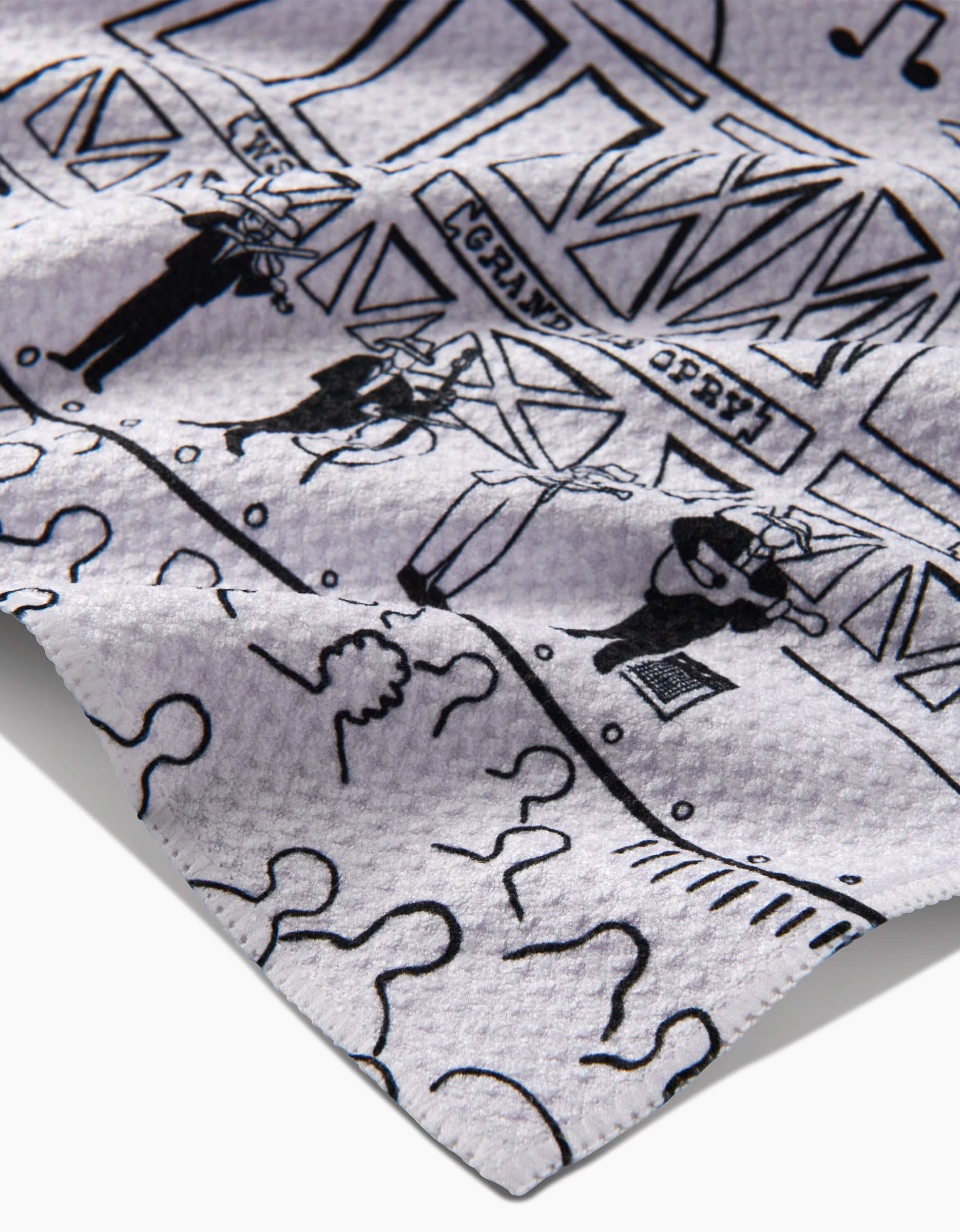 A close-up of the Elisabeth Wing Nashville Tea Towel, crafted with Geoweave™ recycled fabric, displays a black line drawing of people silhouettes, the Grand Ole Opry, and a crowd. Wrinkled texture highlights its unique material.
