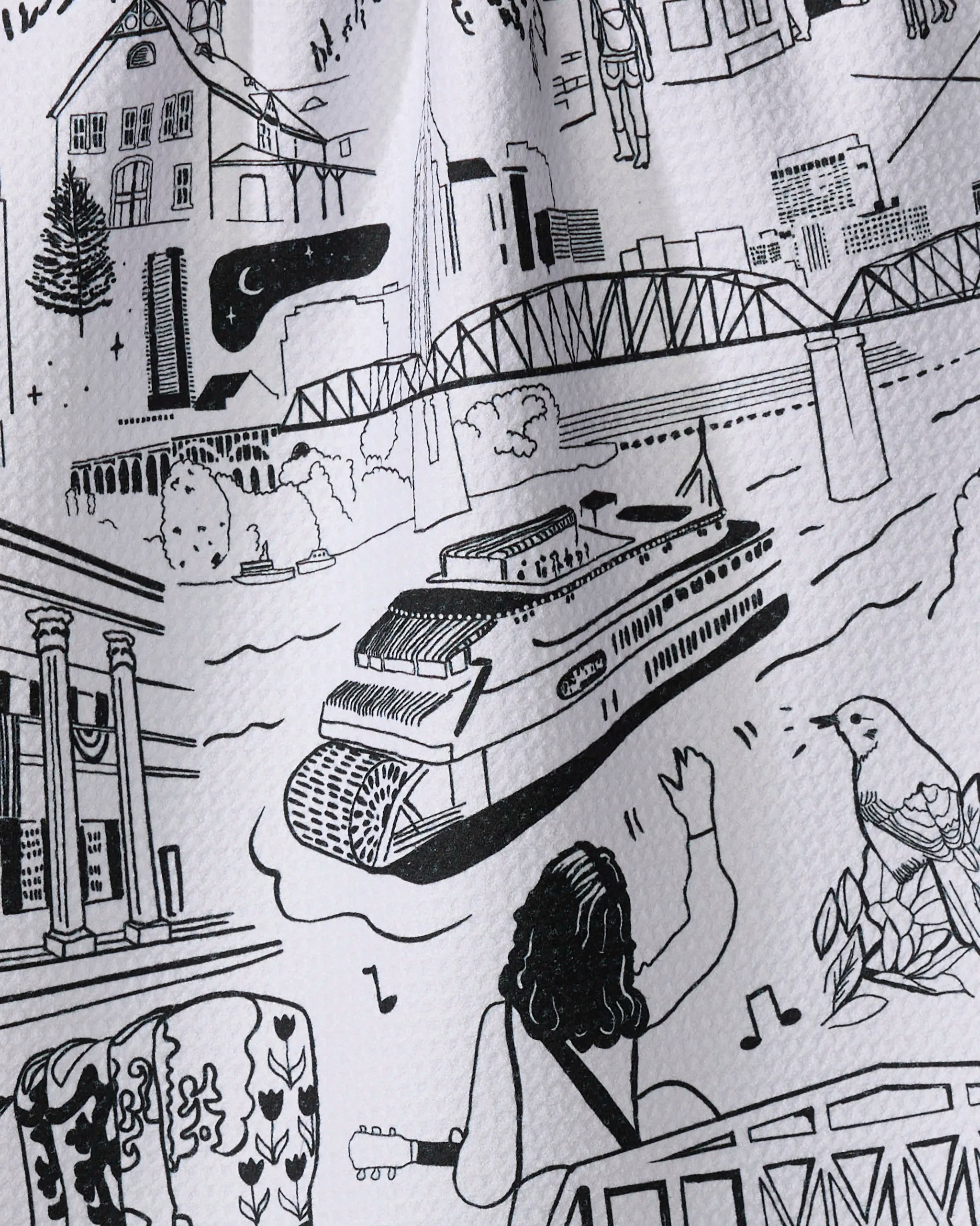 The Elisabeth Wing "Nashville" tea towel features a black and white riverside scene—riverboat, bridge, buildings, guitar player waving, and musical bird—on an ultra-absorbent towel made from recycled materials.