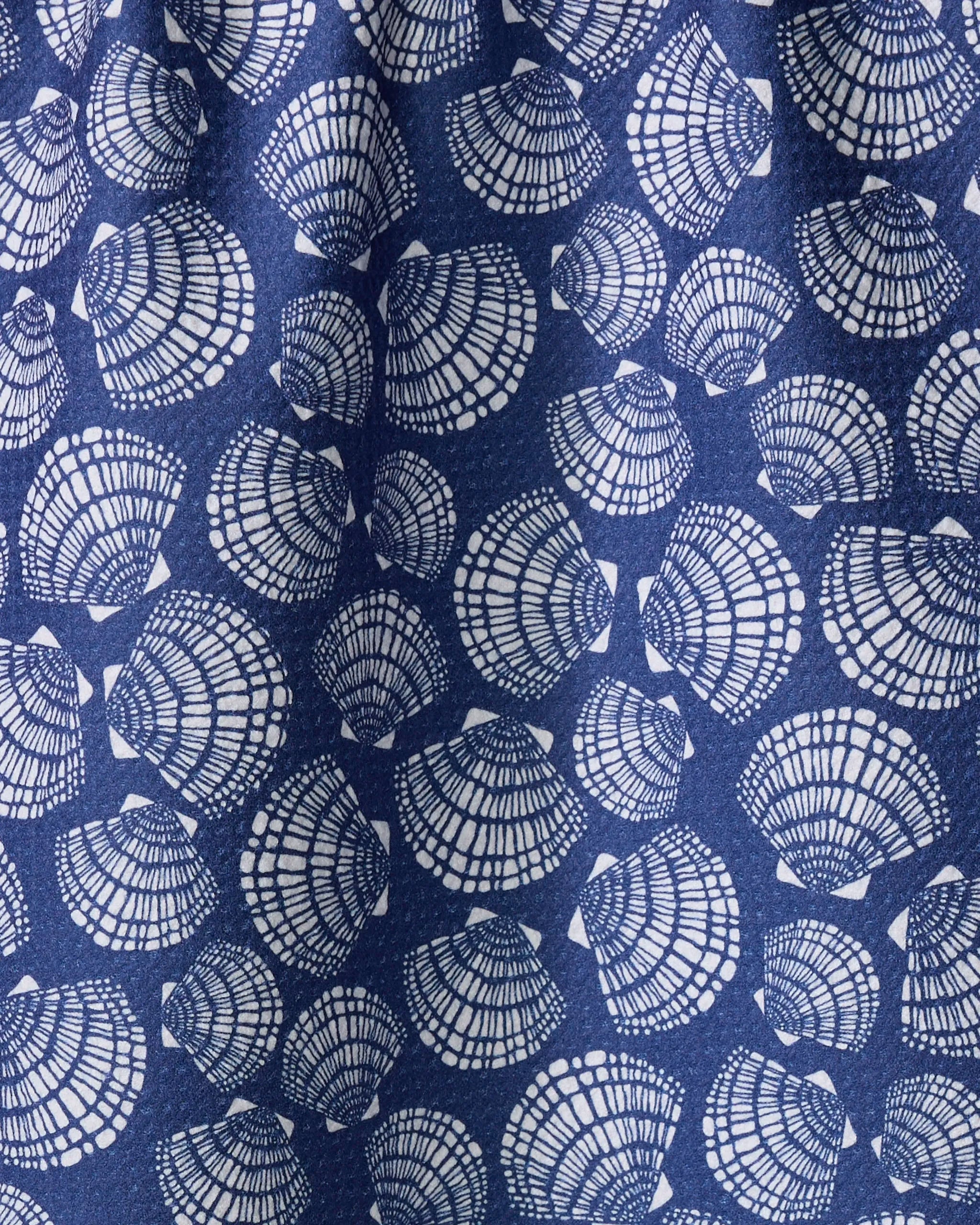 A close-up of Kris Ruff's Nautical Seashells fabric shows blue material with white seashells in various orientations and intricate line details, resembling a quick-drying towel.