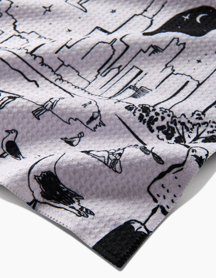 A close-up of ultra-absorbent Geoweave fabric by Elisabeth Wing, New York, featuring black city skyline, crescent moon, trees, birds, and abstract shapes on a recycled waffle-textured surface.