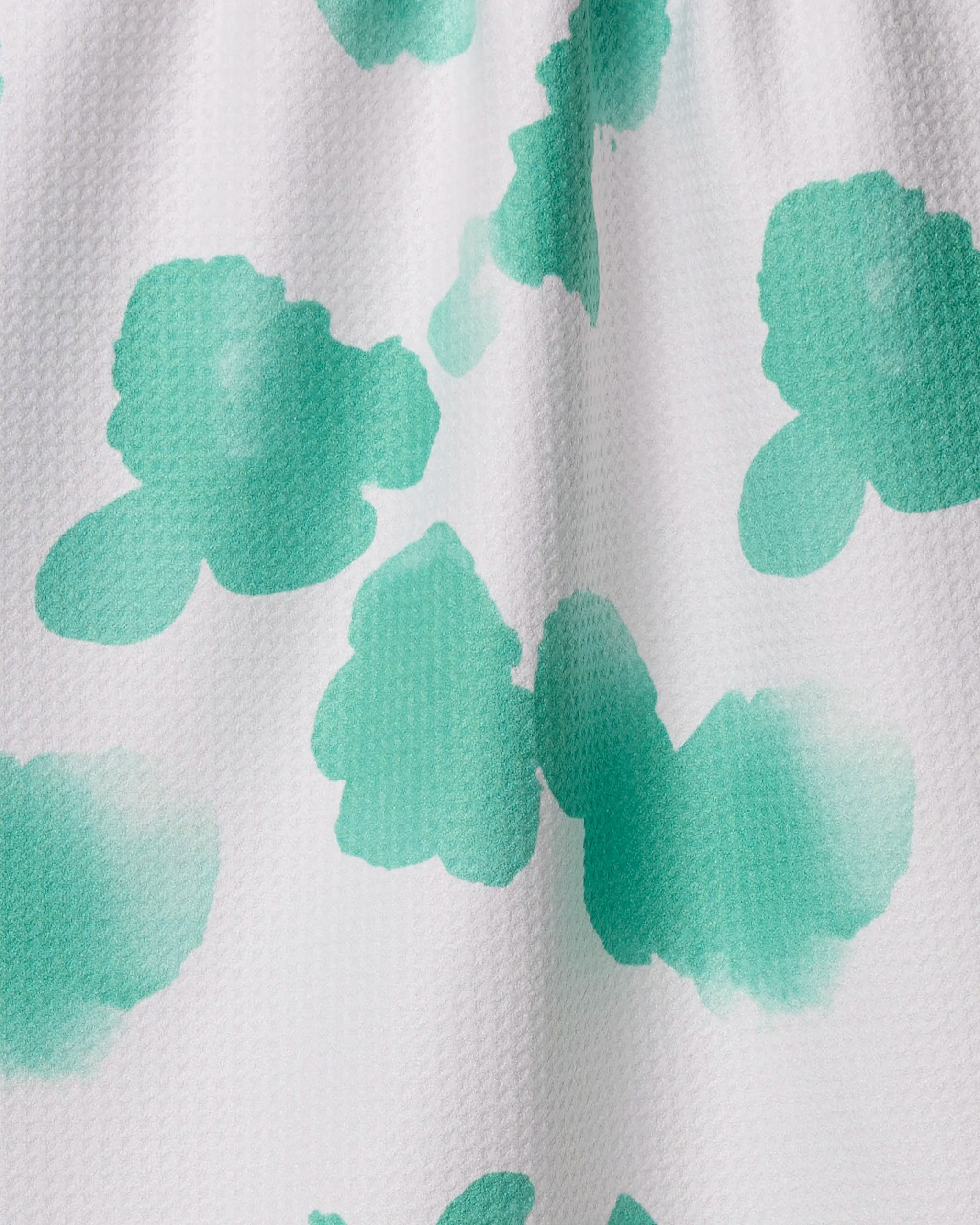 The Geometry Niamh towel features a textured white fabric with abstract green watercolor splotches. Made from recycled materials, it dries quickly and is perfect for your kitchen.