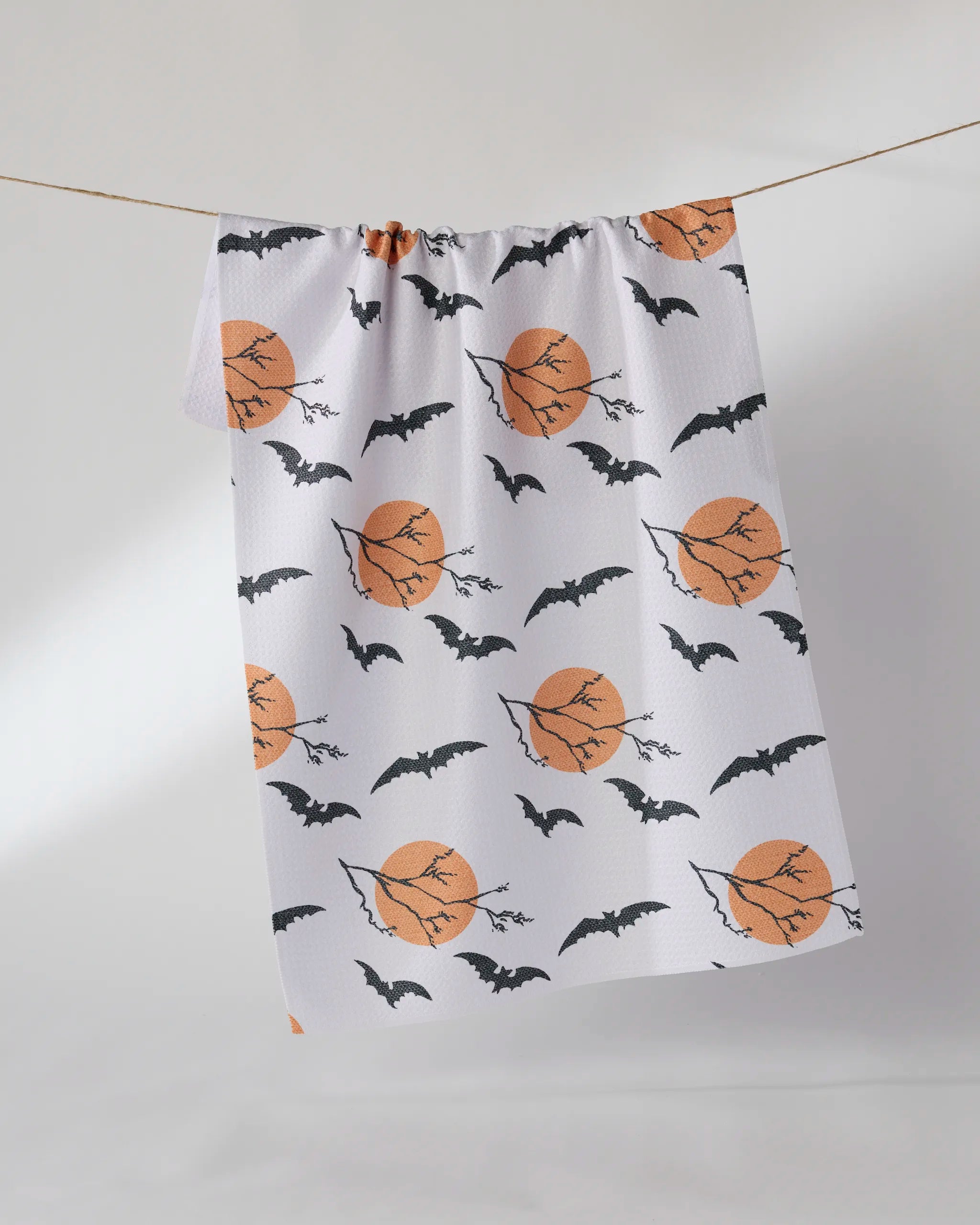 Geometry’s “Night Flight” kitchen towel features a Halloween design with orange full moons and flying black bats on white, perfect for spooky seasonal decor.