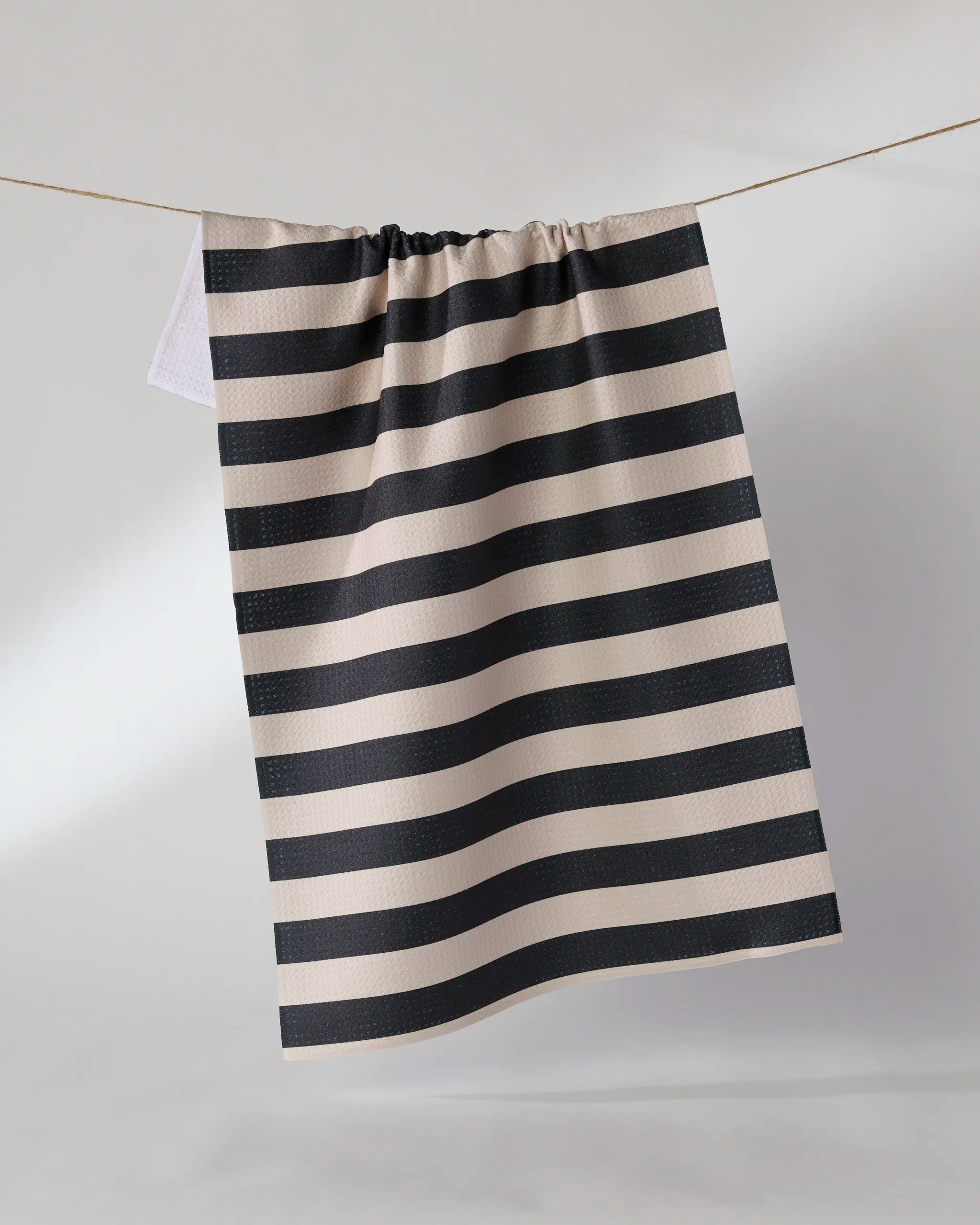 The Geometry "Night Watch" tea towel, featuring black and white stripes, hangs on a clothesline against a plain, light background.