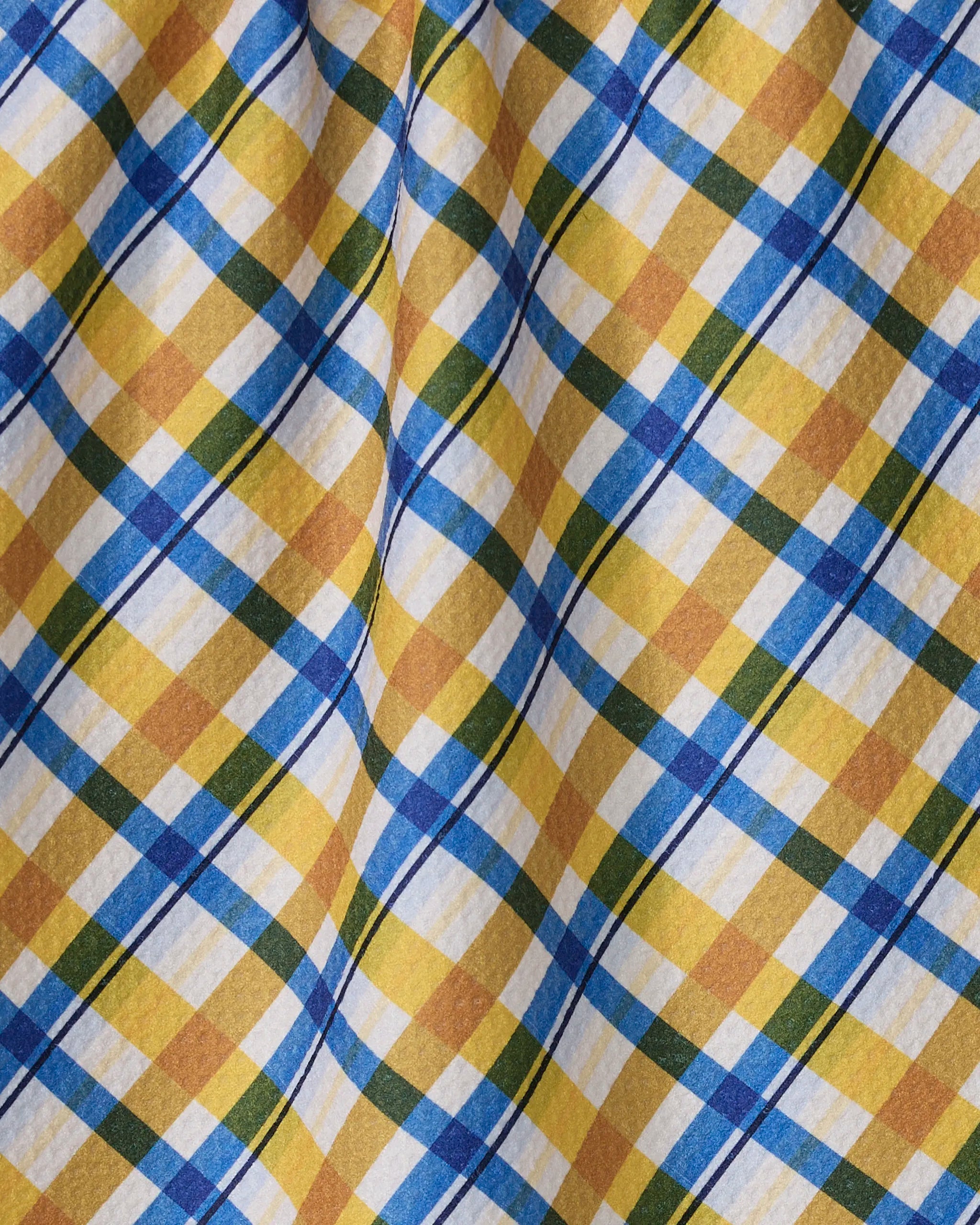 A close-up of the Geometry Nochut recycled kitchen towel, featuring a yellow, blue, white, and brown plaid pattern with diagonal lines and gentle folds in the fabric.