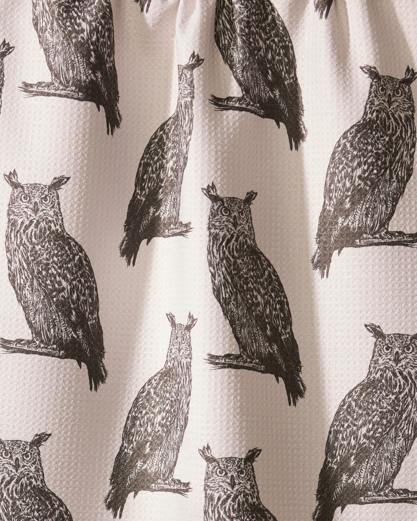 The Geometry Nocturne recycled kitchen towel showcases repeated black owl prints on a light, textured background. A center owl is uniquely distorted by a fabric fold.