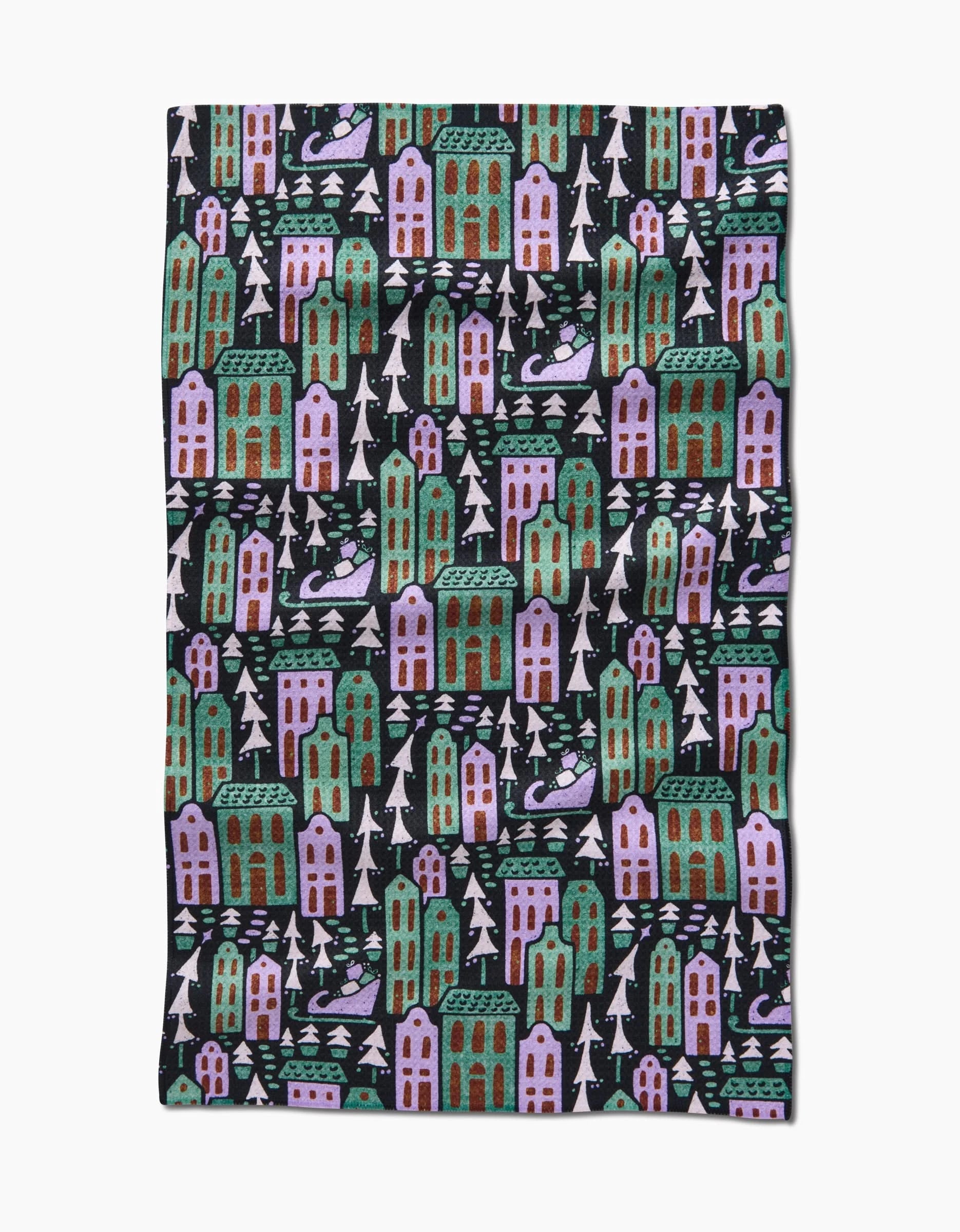 The Noelle tea towel by Amy MacCready features tall houses in green, purple, and pink with white trees on a black background. Made from recycled materials for an eco-friendly touch.