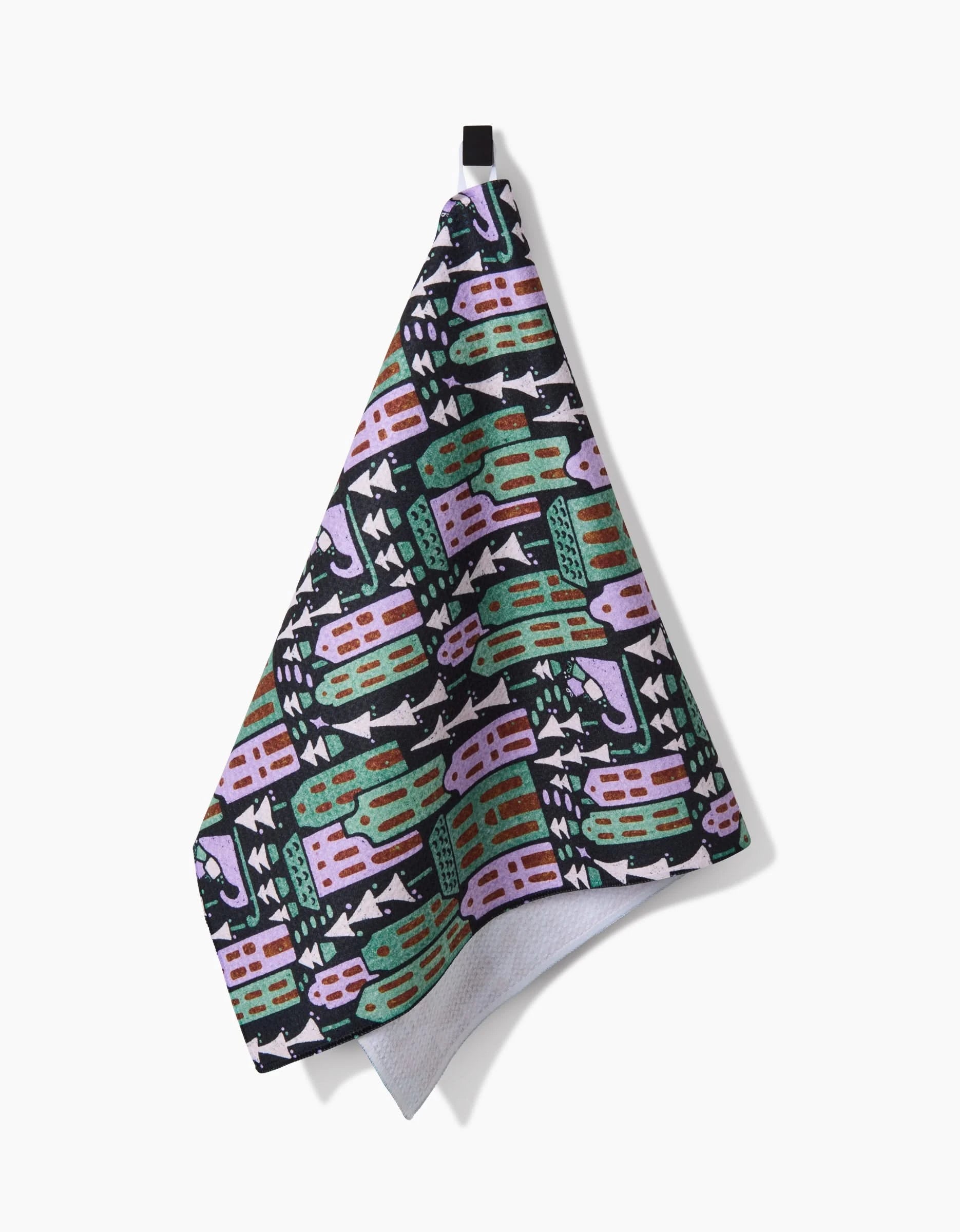 The Noelle tea towel by Amy MacCready is ultra-absorbent with a colorful geometric pattern in pink, green, black, and white, hanging from a black loop against a white background.