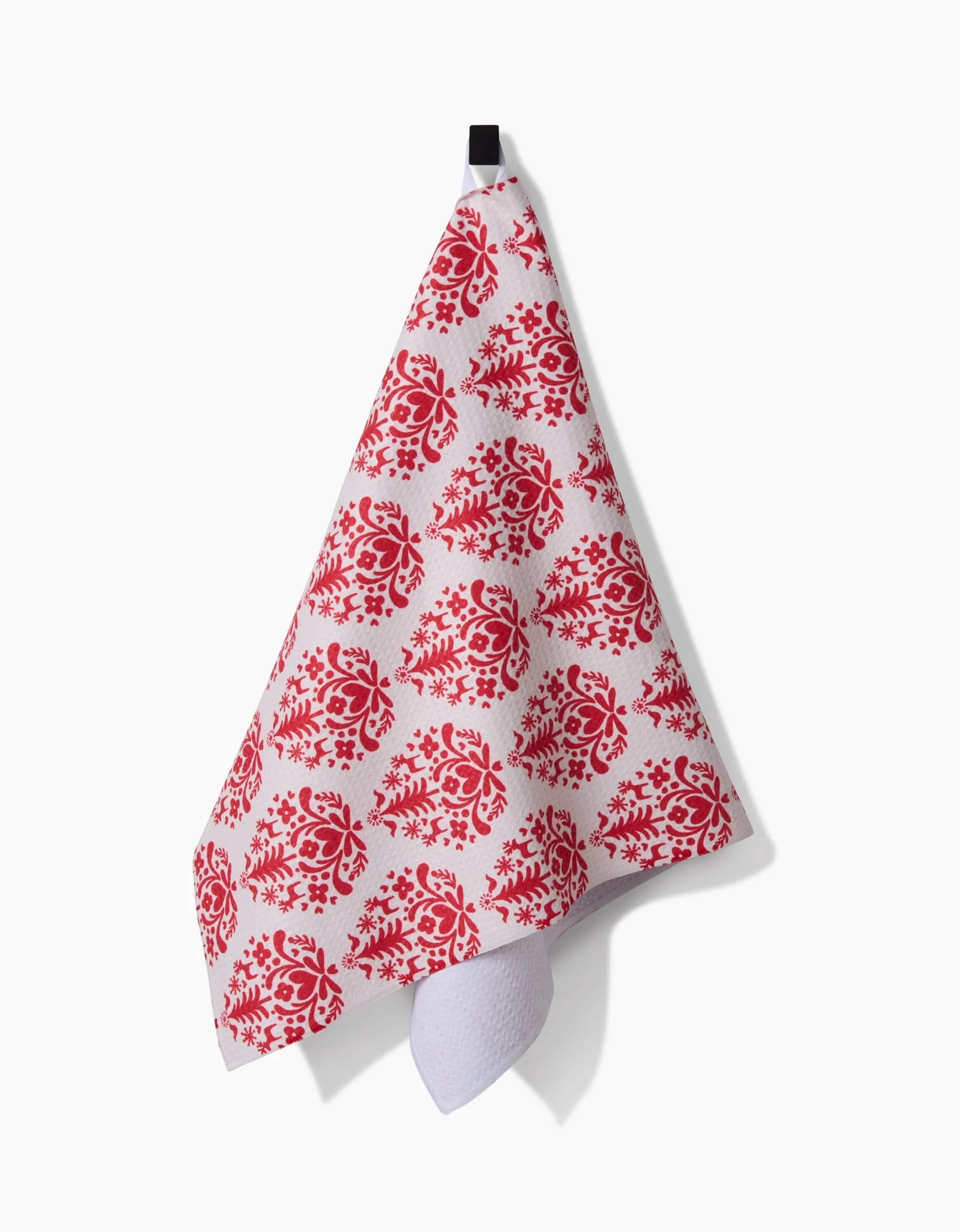 The Nordic Holiday Stamp tea towel by Kayla Ann, made from recycled materials, features a red floral pattern on white and hangs from a black hook with one corner pointing down.