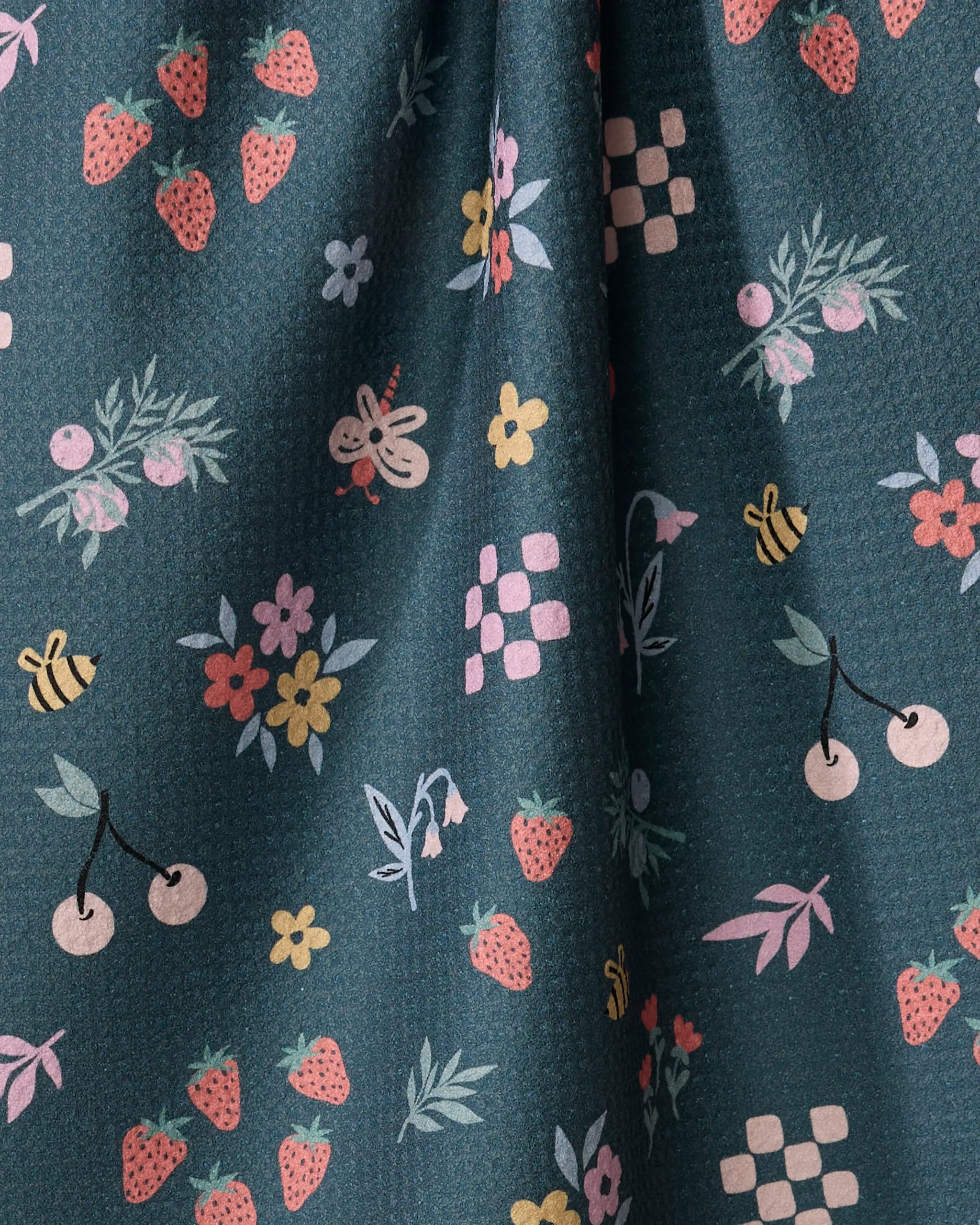 The North Meadow tea towel by Charlie Rowan Designs features a whimsical, quick-drying teal design with strawberries, bees, cherries, flowers, leafy branches, and pink-and-white checkerboard motifs throughout.