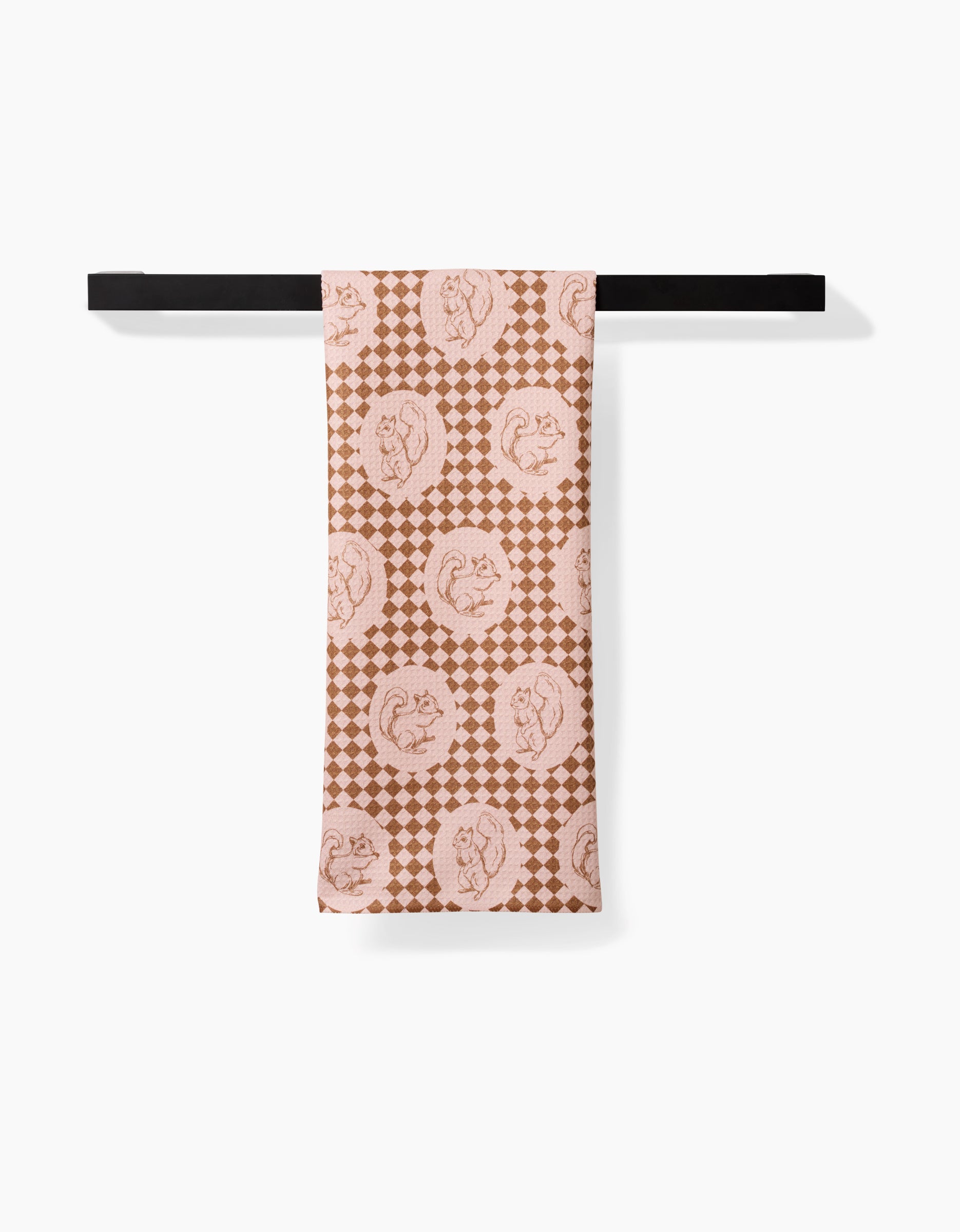The Nuts About You tea towel by Aubrey Fairchild features brown and beige squirrels and checkered circles on quick-drying recycled material, hanging neatly on a slim black rod against a white background.
