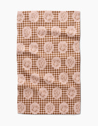 The “Nuts About You” tea towel by Aubrey Fairchild features a brown and beige circular squirrel design over small diamonds. Made of quick-drying fabric, it appears slightly wrinkled and is displayed on a white surface.