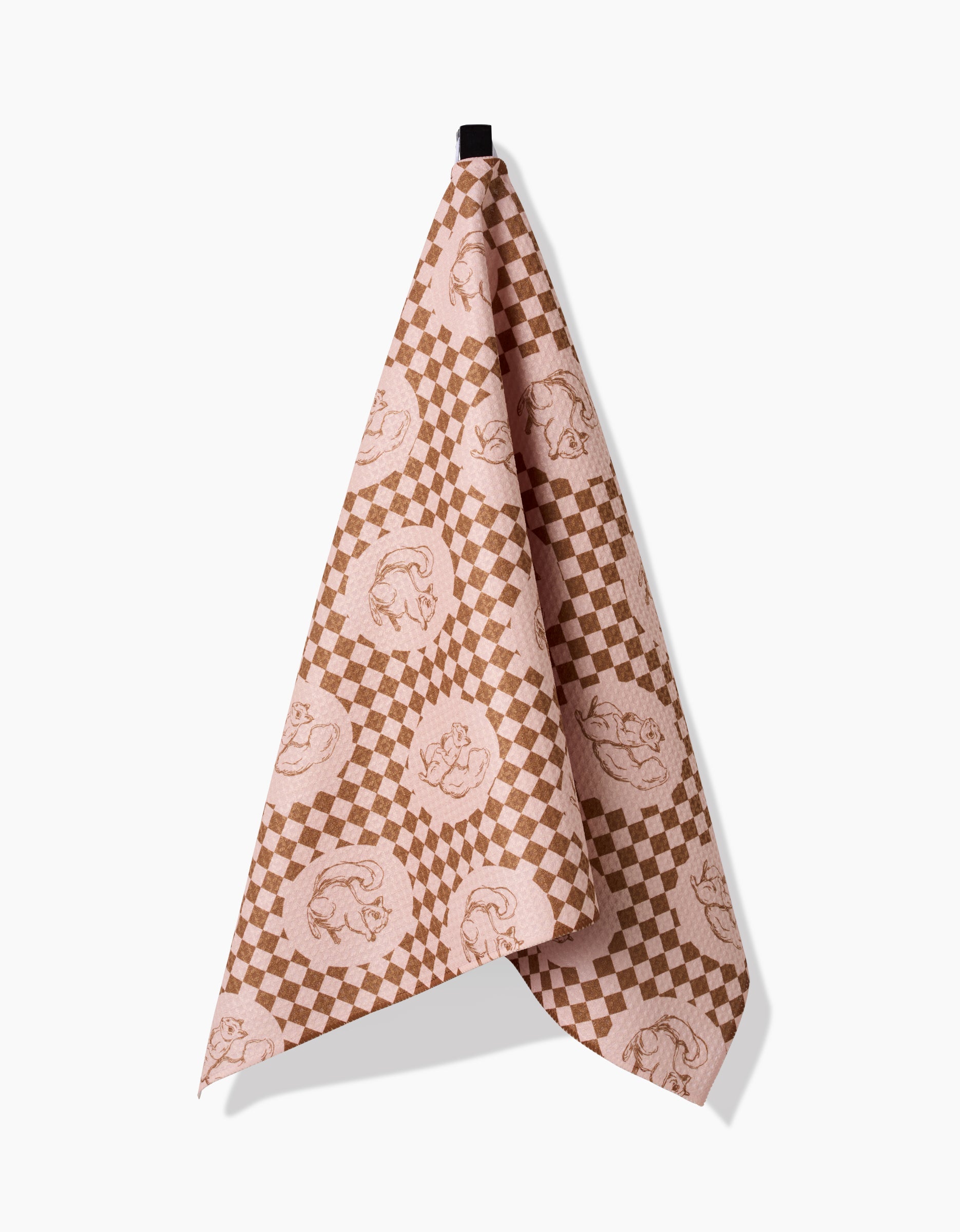The Aubrey Fairchild Nuts About You tea towel, featuring pink and brown checkered circles and made from recycled materials, hangs on a black hook against a plain white background.
