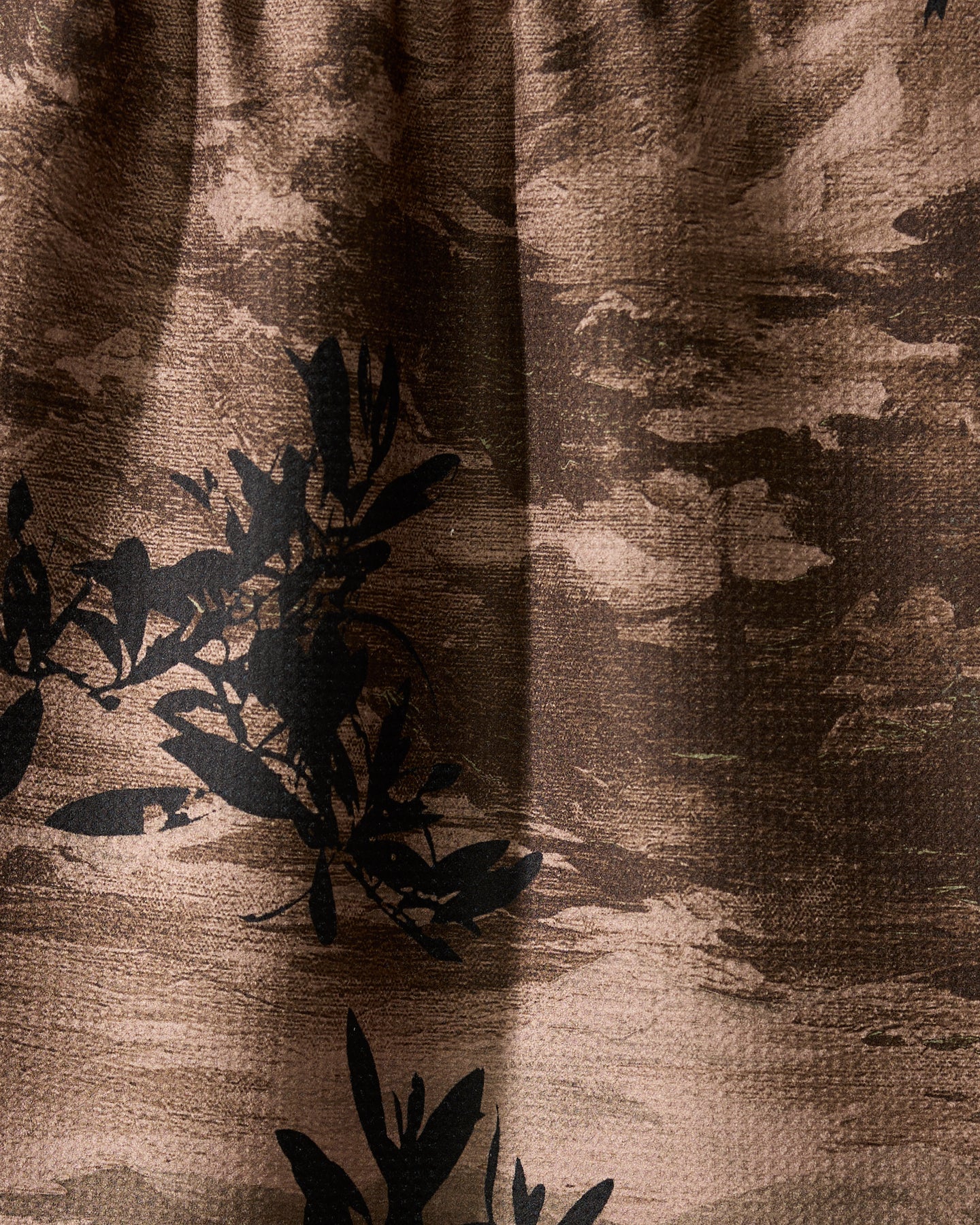 Close-up of Geometry’s Oaklen tea towel, crafted from recycled materials. The brown, ultra-absorbent fabric features a textured surface with black leafy branch patterns and abstract cloud-like shapes in lighter brown tones.