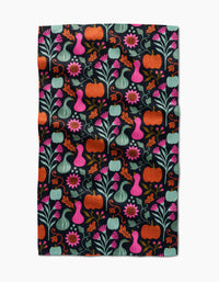 The Oakley kitchen towel by Amy MacCready features a vibrant folk art design of pumpkins, gourds, flowers, and leaves in orange, pink, teal, and green on a black background for a whimsical touch.