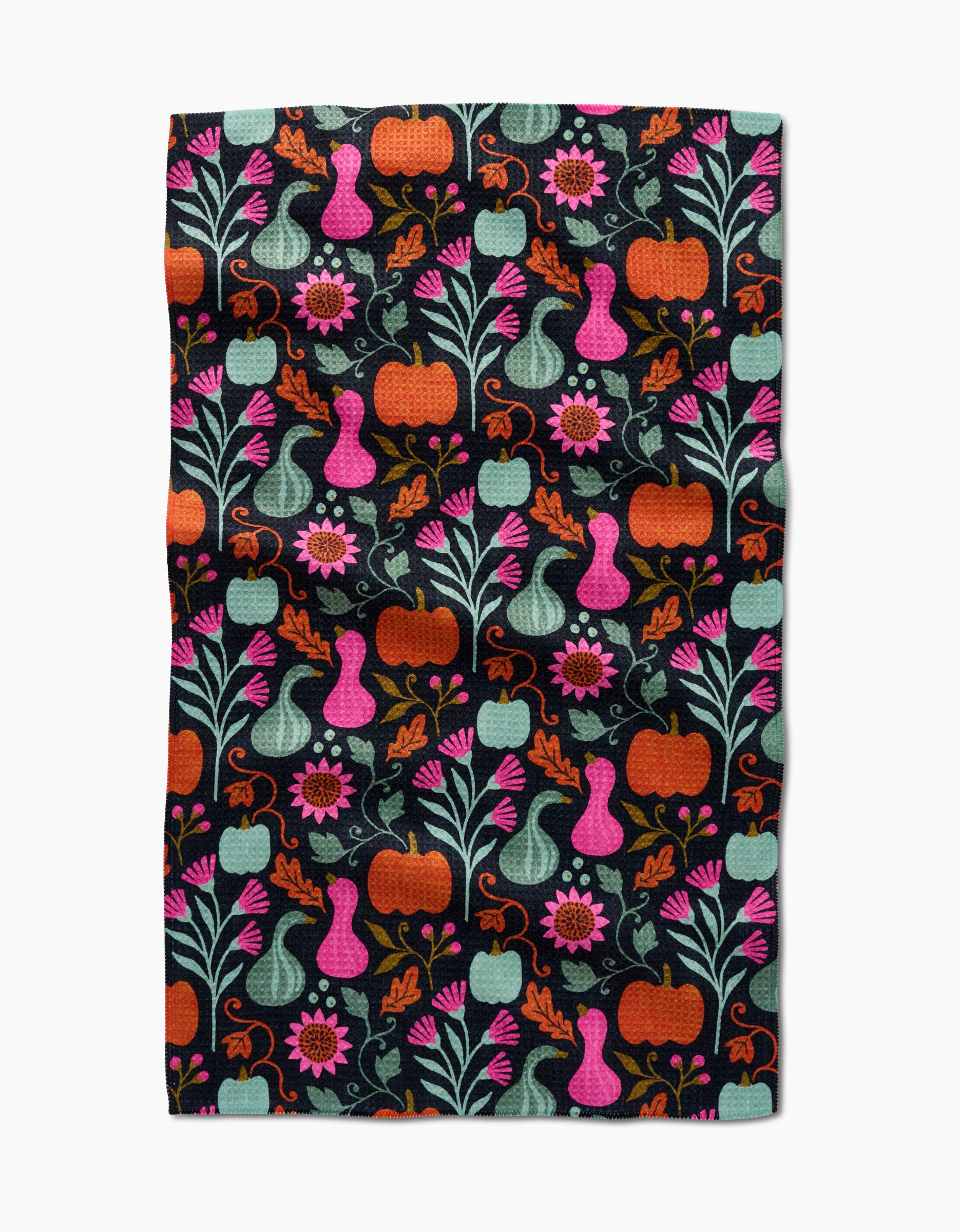 The Oakley kitchen towel by Amy MacCready features a vibrant folk art design of pumpkins, gourds, flowers, and leaves in orange, pink, teal, and green on a black background for a whimsical touch.