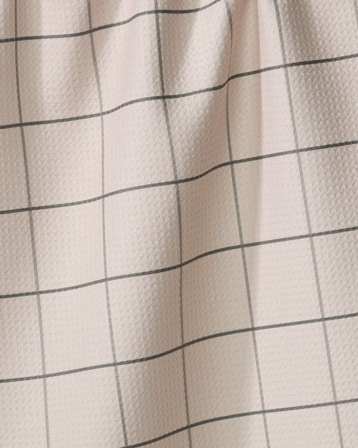 The Oat Grid tea towel by Kelsi Fullmer features a light pink hue and black grid pattern. Made from recycled materials, it has gentle folds and a softly textured, dimpled surface.