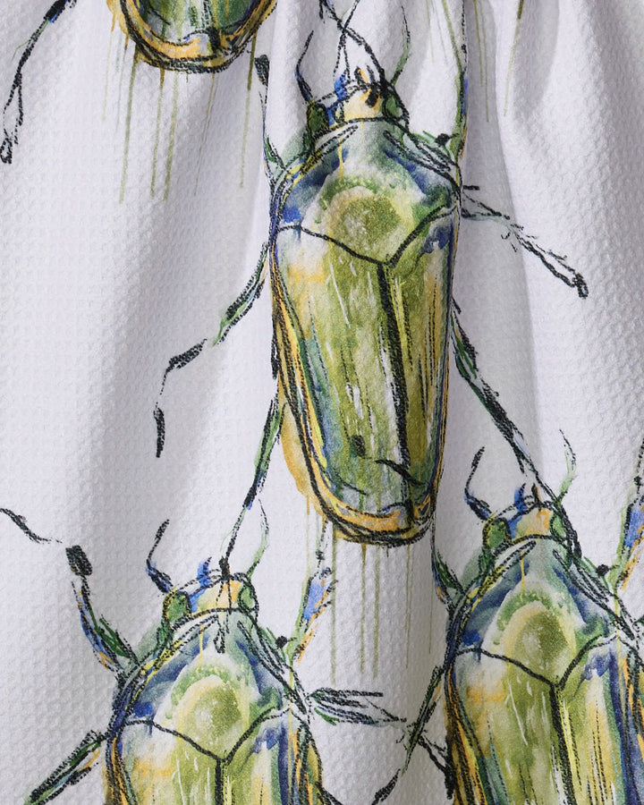 A close-up of the Olive Beetles tea towel by Taryn Brennan, showcasing a white textured fabric with green and yellow beetle illustrations outlined in dark lines in a scattered, overlapping pattern.