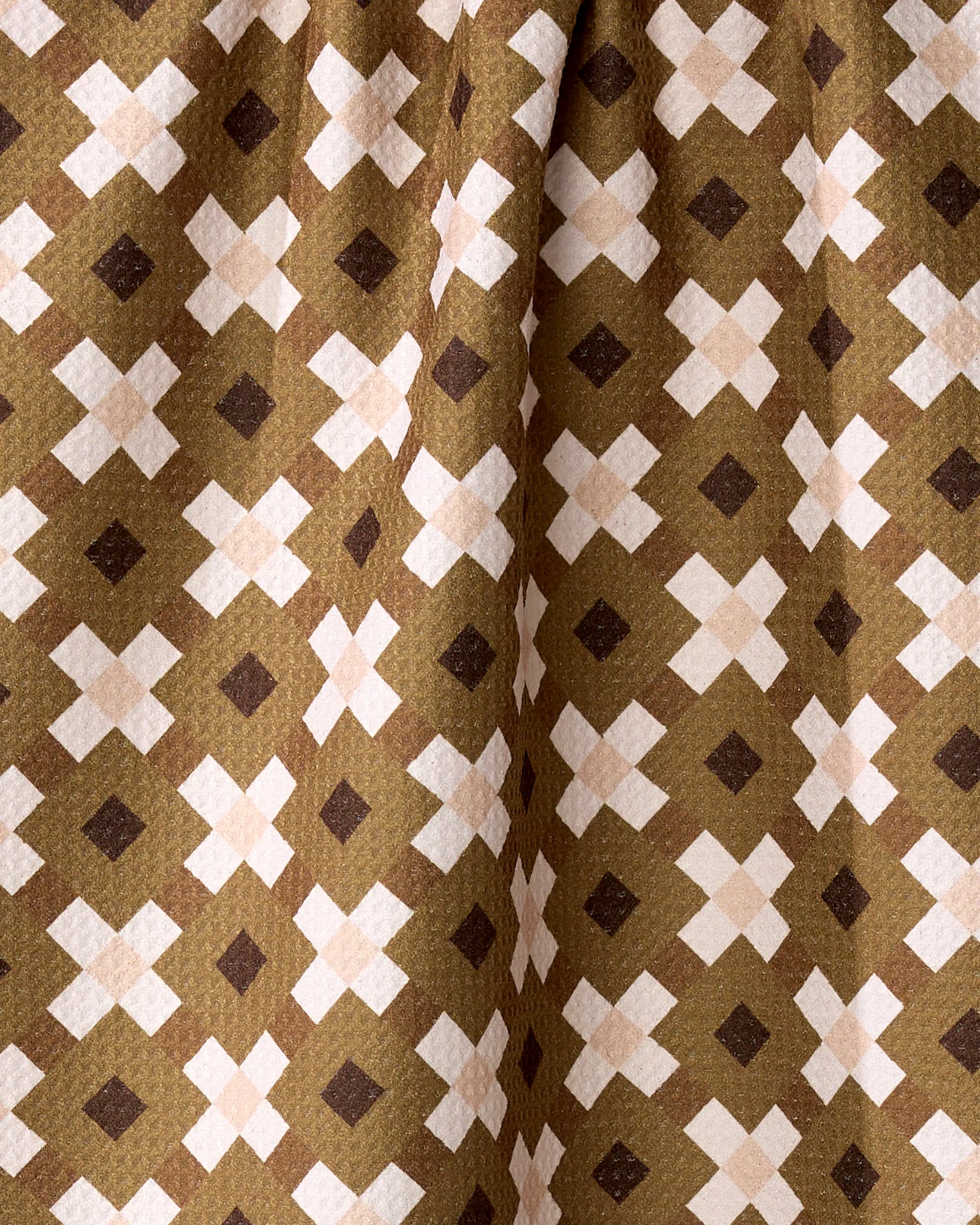 A close-up of Teri the Butter’s Olive Geo recycled kitchen towel, featuring a repeating geometric pattern of white and dark brown X shapes on a light brown, slightly pleated fabric.