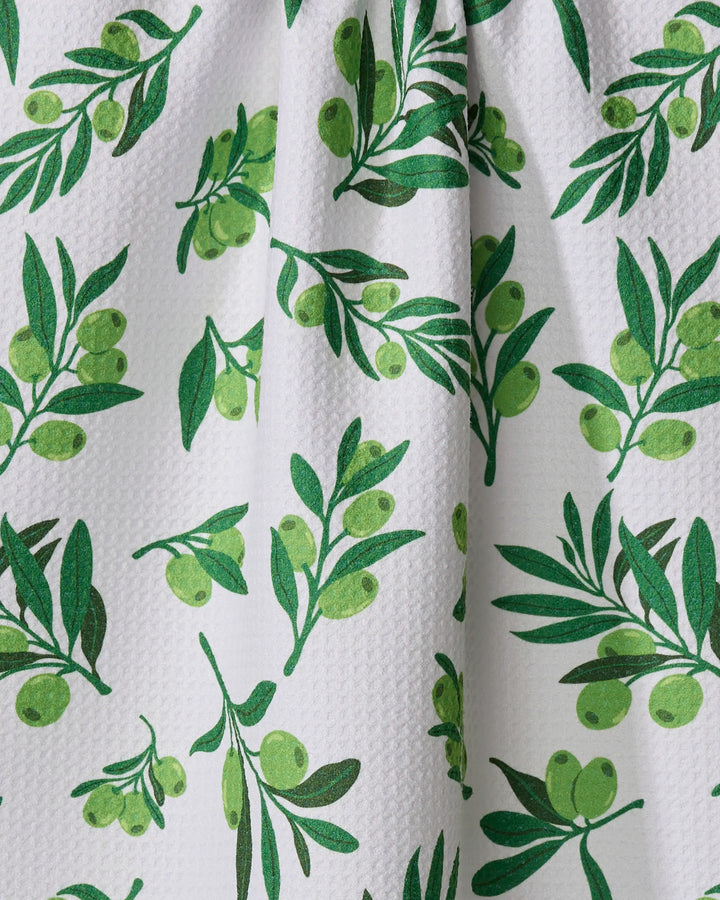 The Olive Grove tea towel by Vaishali Design Studio features a white textured surface adorned with a repeating green olive branch pattern, complete with leaves and olive clusters.