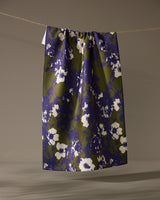 The Oliveberry skirt by Geometry, knee-length with a gathered waistband, made from quick-drying recycled materials and adorned with a blue and olive green abstract floral print, hangs from a clothesline against a neutral background.