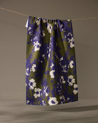 The Oliveberry skirt by Geometry, knee-length with a gathered waistband, made from quick-drying recycled materials and adorned with a blue and olive green abstract floral print, hangs from a clothesline against a neutral background.