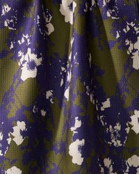 A close-up of Geometrys Oliveberry tea towel, crafted from quick-drying recycled materials. It features a softly pleated, textured surface with an abstract floral pattern in white, purple, and olive green.