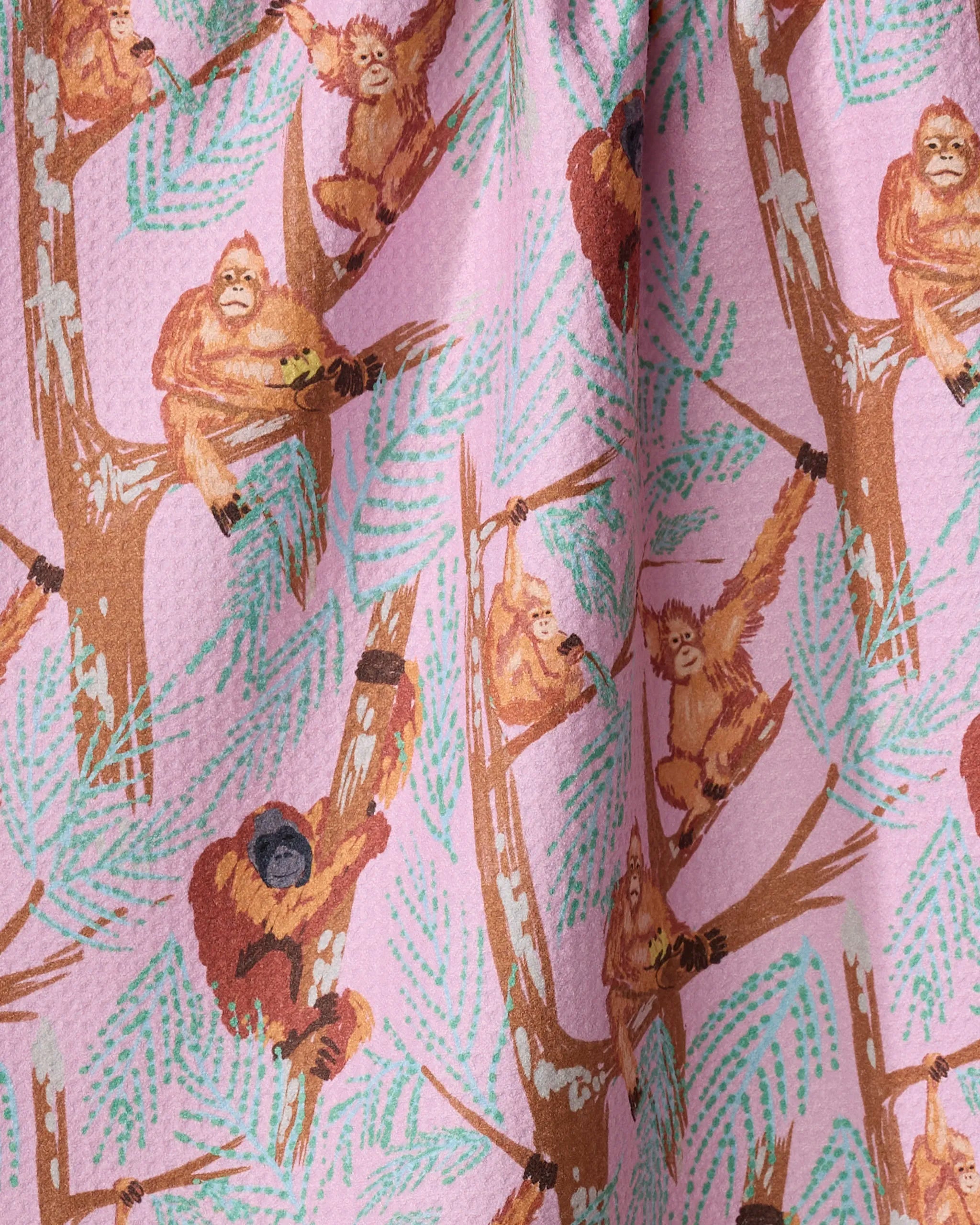 Orangutan Clan tea towel by Elisabeth Wing features orangutans swinging and sitting on leafy brown branches against a light pink background. The textured, gathered fabric adds charm to your kitchen décor.