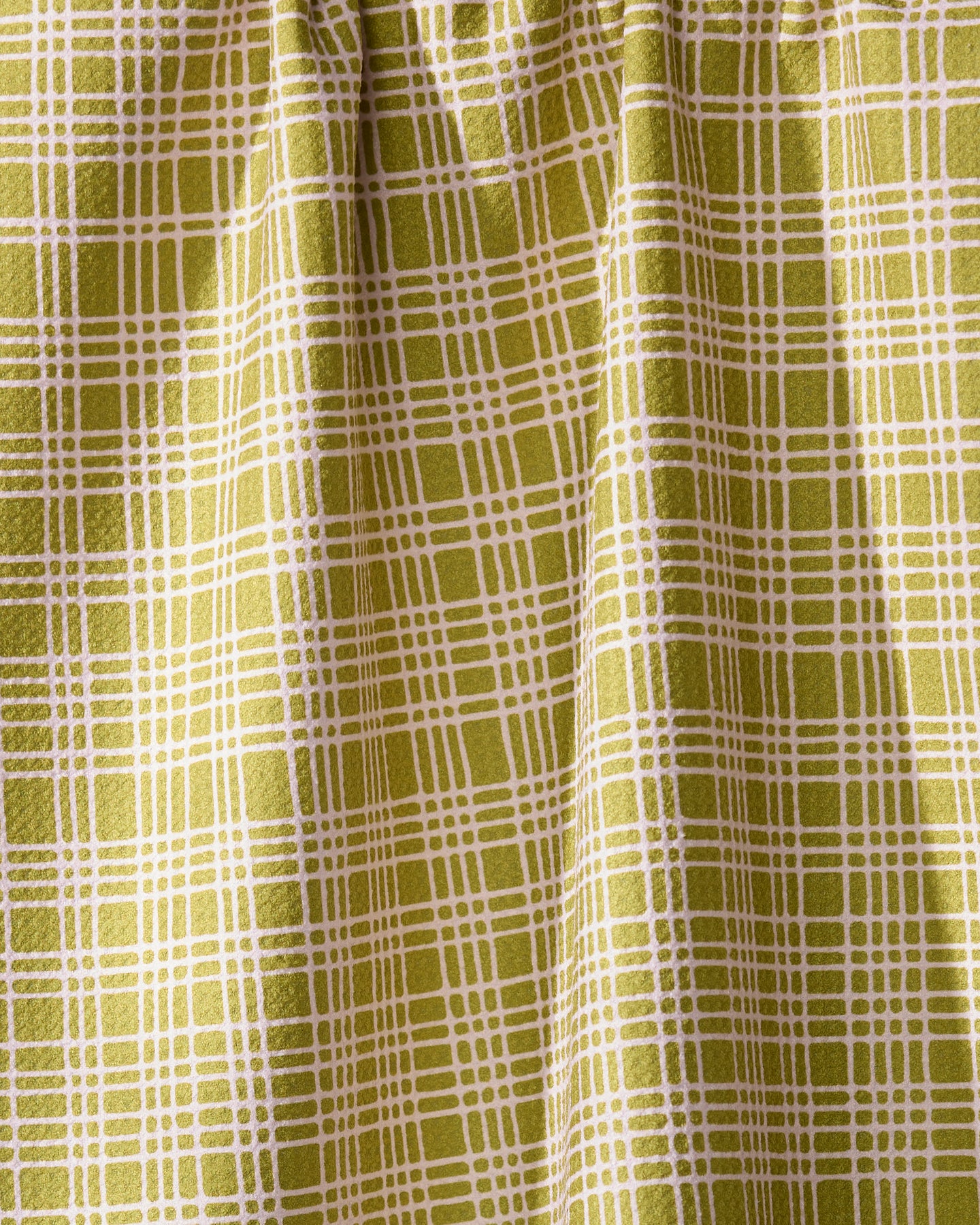 A detailed view of Geometry’s Orchard Plaid Green curtain features a yellow-green grid reminiscent of a tea towel. The eco-friendly fabric is gathered at the top, forming soft vertical folds.