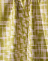 A detailed view of Geometry’s Orchard Plaid Green curtain features a yellow-green grid reminiscent of a tea towel. The eco-friendly fabric is gathered at the top, forming soft vertical folds.