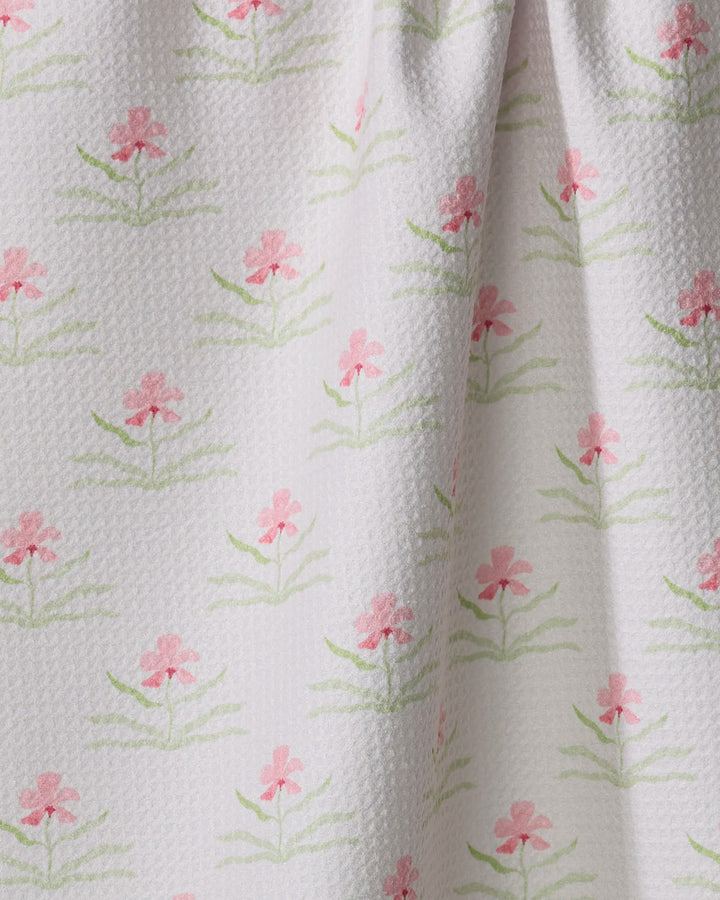 A close-up of Laura Prietto’s Orchids In Bloom fabric shows a repeating pattern of pink flowers and green leaves on textured white, crafted from quick-drying material and softly gathered at the top.