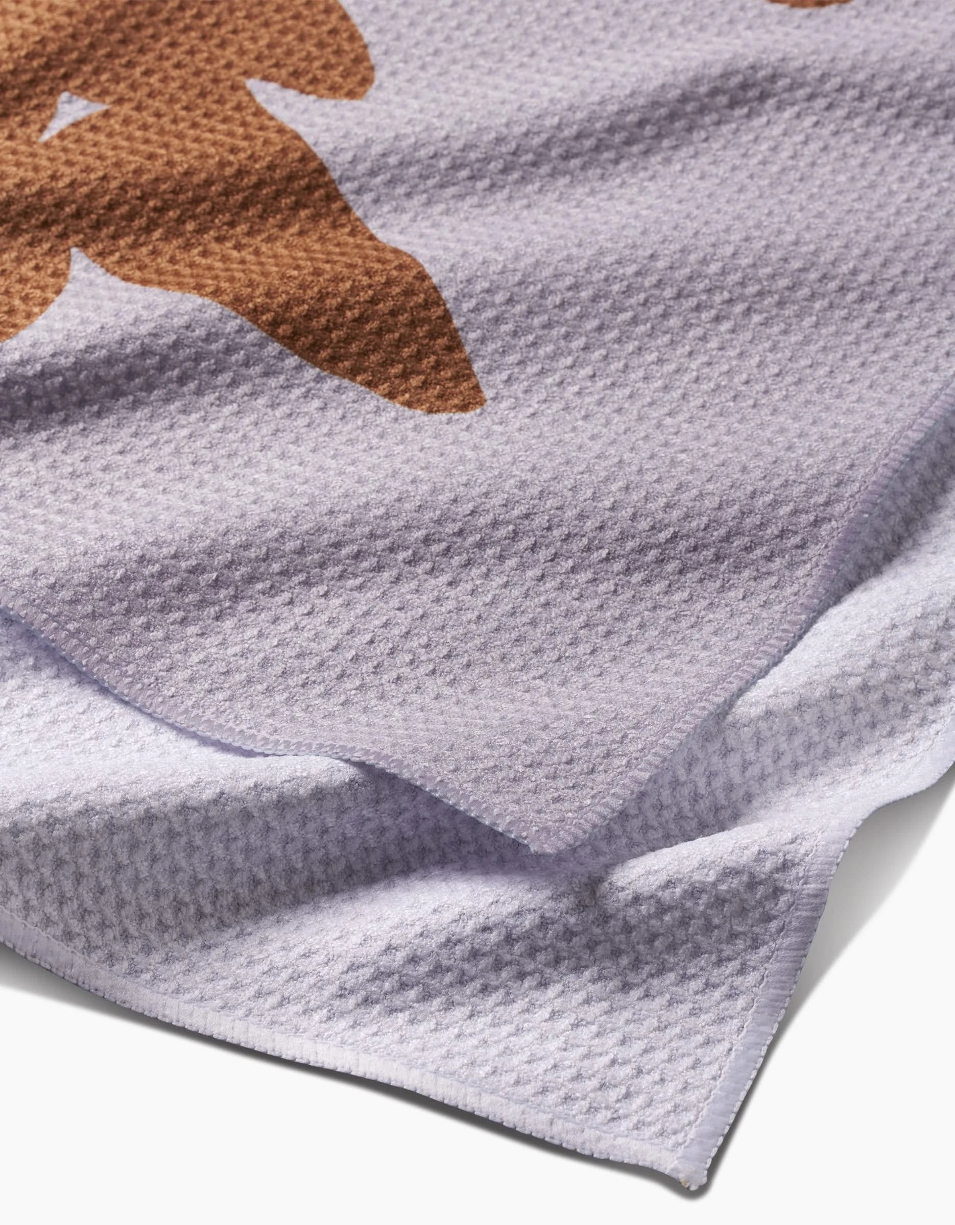 A close-up of PrintedPlants Oregano Tea Towel shows its light purple Geoweave™ fabric, brown leaf-like pattern, soft waffle weave texture, and neatly finished edges.