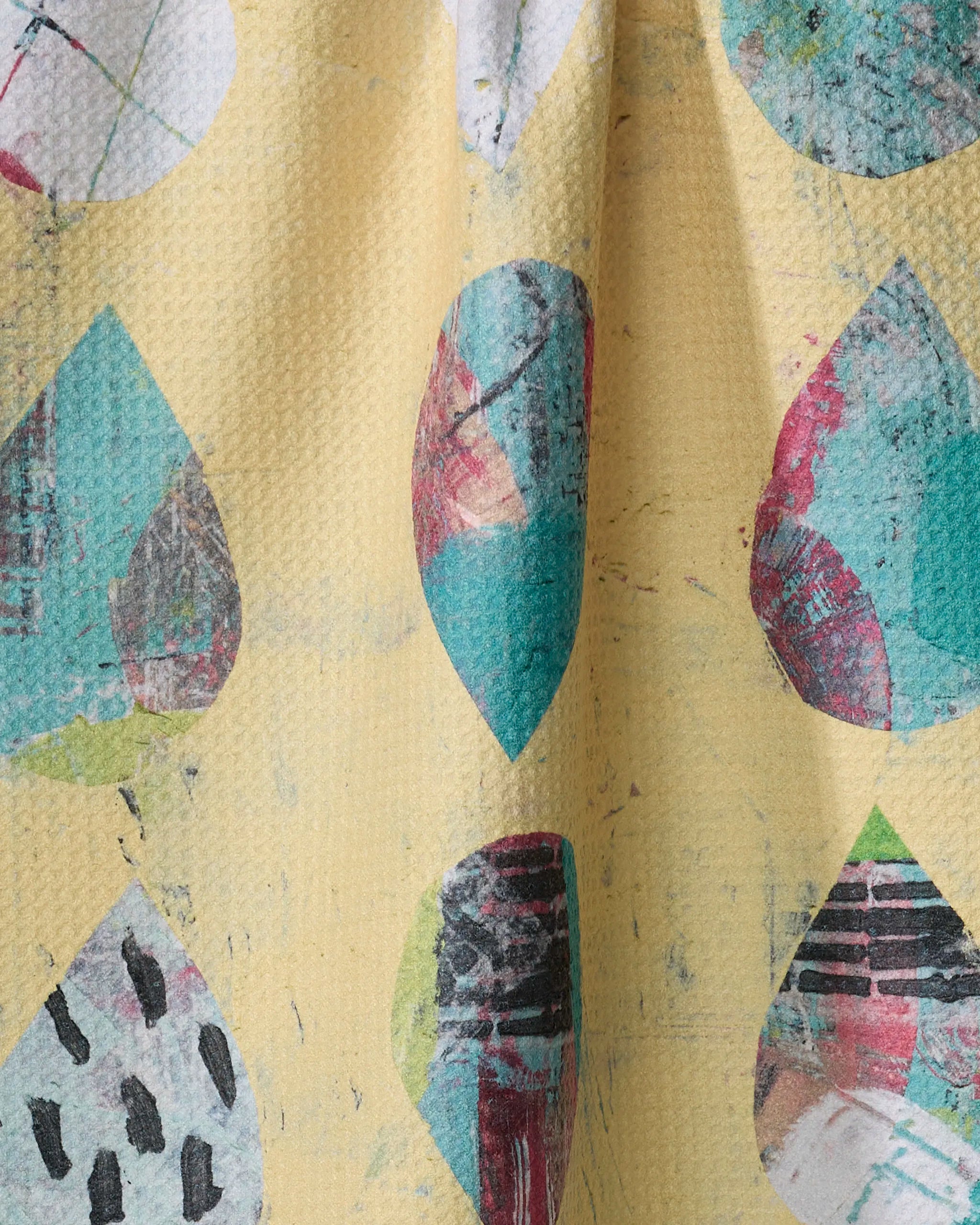 Close-up of the "Outer Limits" tea towel by Katherine Berkeley, featuring a textured yellow background with colorful abstract teardrop shapes in teal, red, black, and white for an artistic, quick-drying finish.