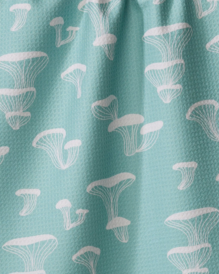 The Amberleigh Adoff Oyster Shroom is a light blue textured kitchen tea towel featuring a white stylized mushroom pattern. Made from recycled materials, this ultra-absorbent towel brightens up any kitchen.
