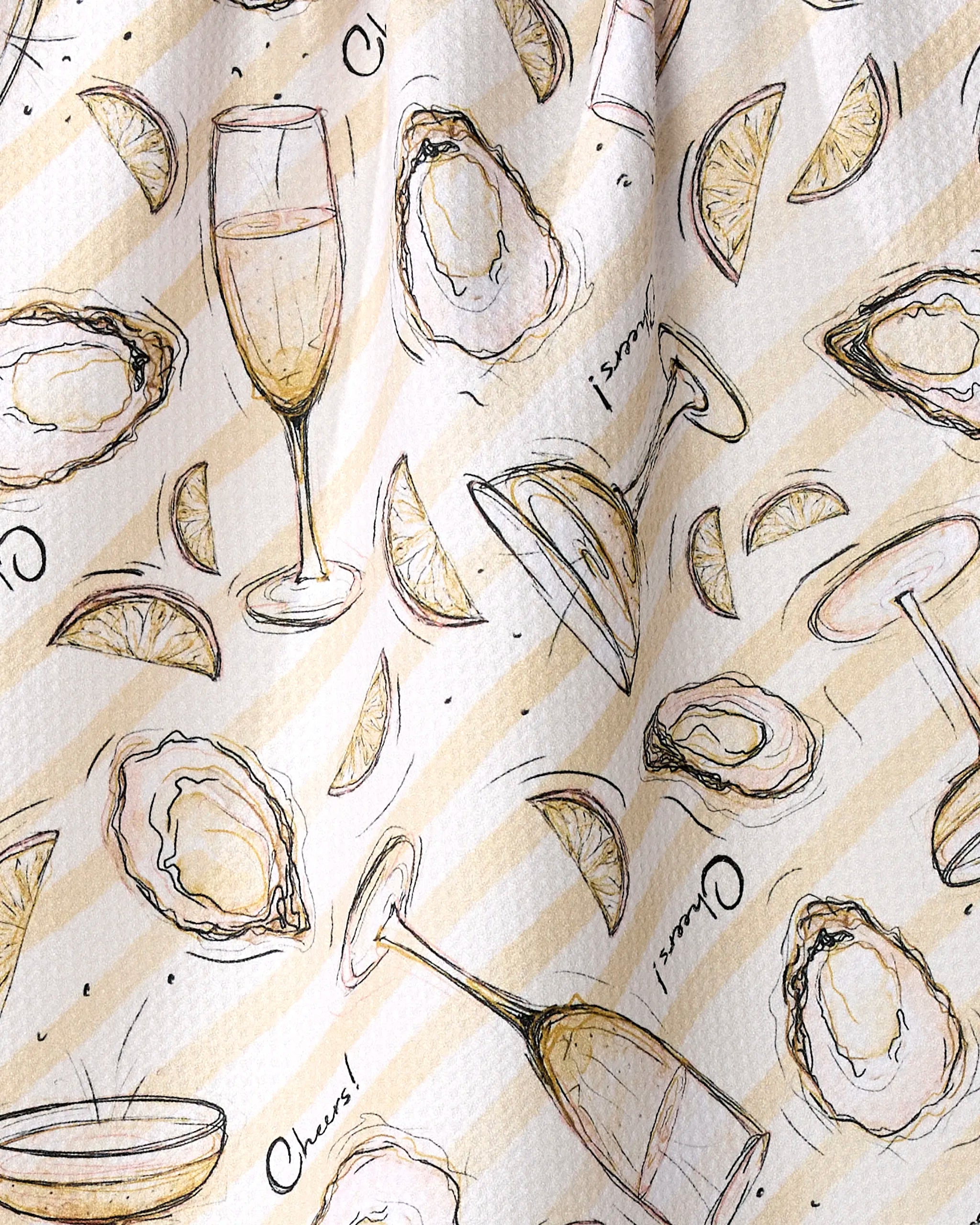 The Geometry Oysters and Champagne recycled kitchen towel features oyster, lemon wedge, champagne flute, and coupe glass illustrations with “Cheers!” text on a beige striped background.