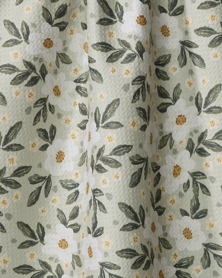 A close-up of Painted Spring Flowers dish towel by Teri the Butter shows textured, absorbent light green fabric with white flowers, yellow centers, small yellow dots, and green leaves.