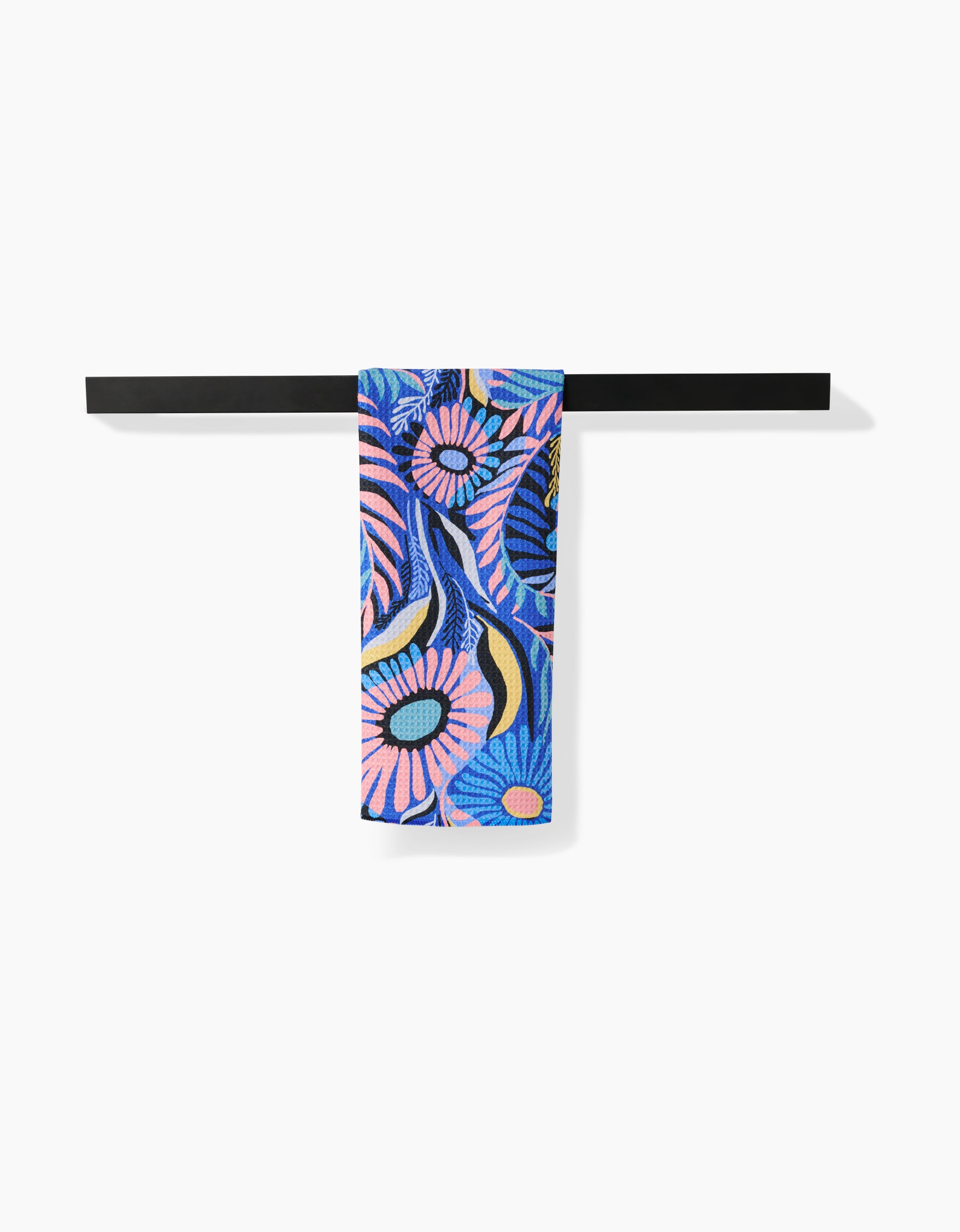 The Masha Volnova Palm Beach Geoweave™ tea towel, featuring a vibrant blue, pink, and yellow floral pattern, hangs neatly on a black horizontal towel bar against a white background.