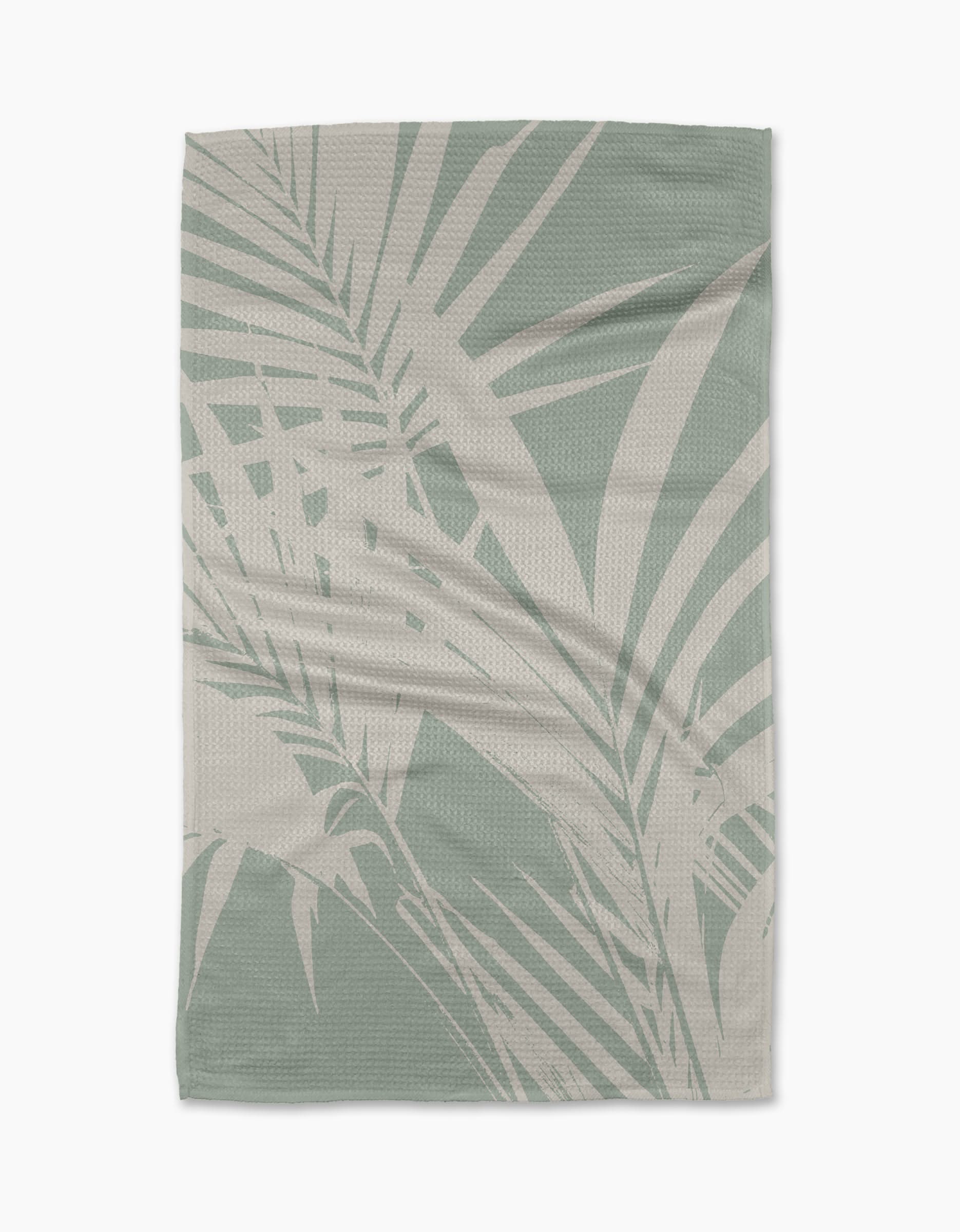 The Palm Breeze blanket by Geometry features a light green and beige palm leaf pattern on durable Geoweave fabric, creating a tropical, modern look. Shown laid flat on a white background.