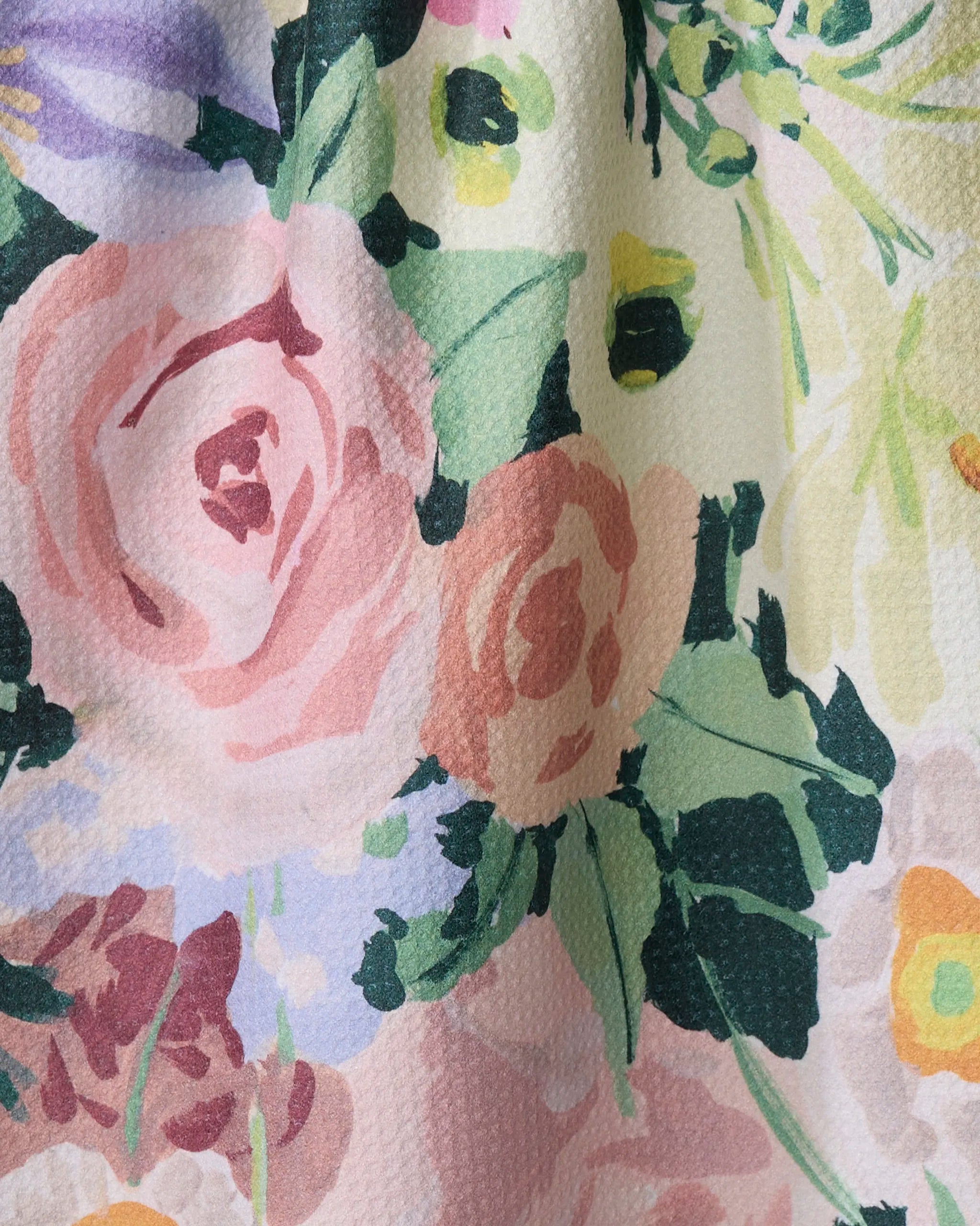 A close-up of the "Pastel Bouquet" kitchen towel by Ania Zwara Art, showcasing a textured fabric with a colorful floral pattern of pink roses, green leaves, and touches of purple and yellow flowers.