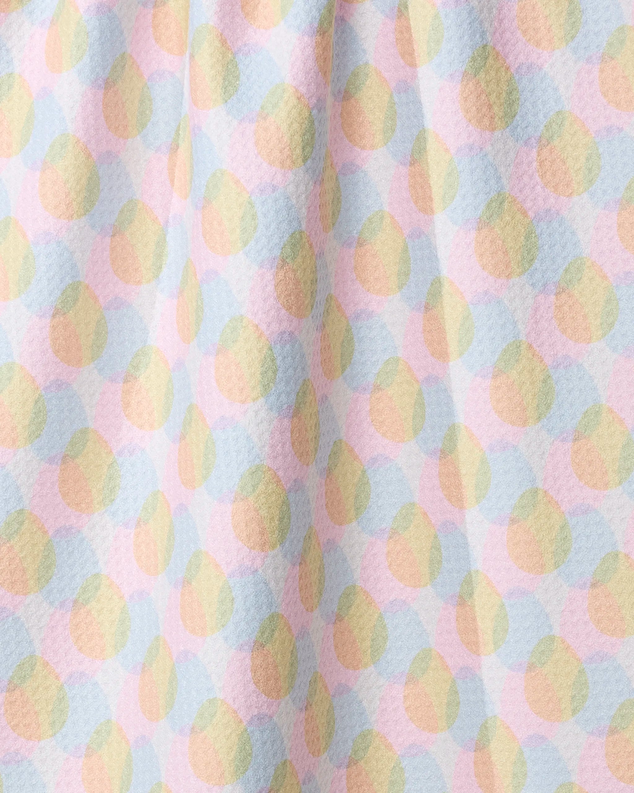 A close-up of Geometry's Pastel Pop tea towel, softly draped and crafted from recycled materials, featuring textured fabric adorned with pastel overlapping circles in pink, yellow, green, and blue on a light background.