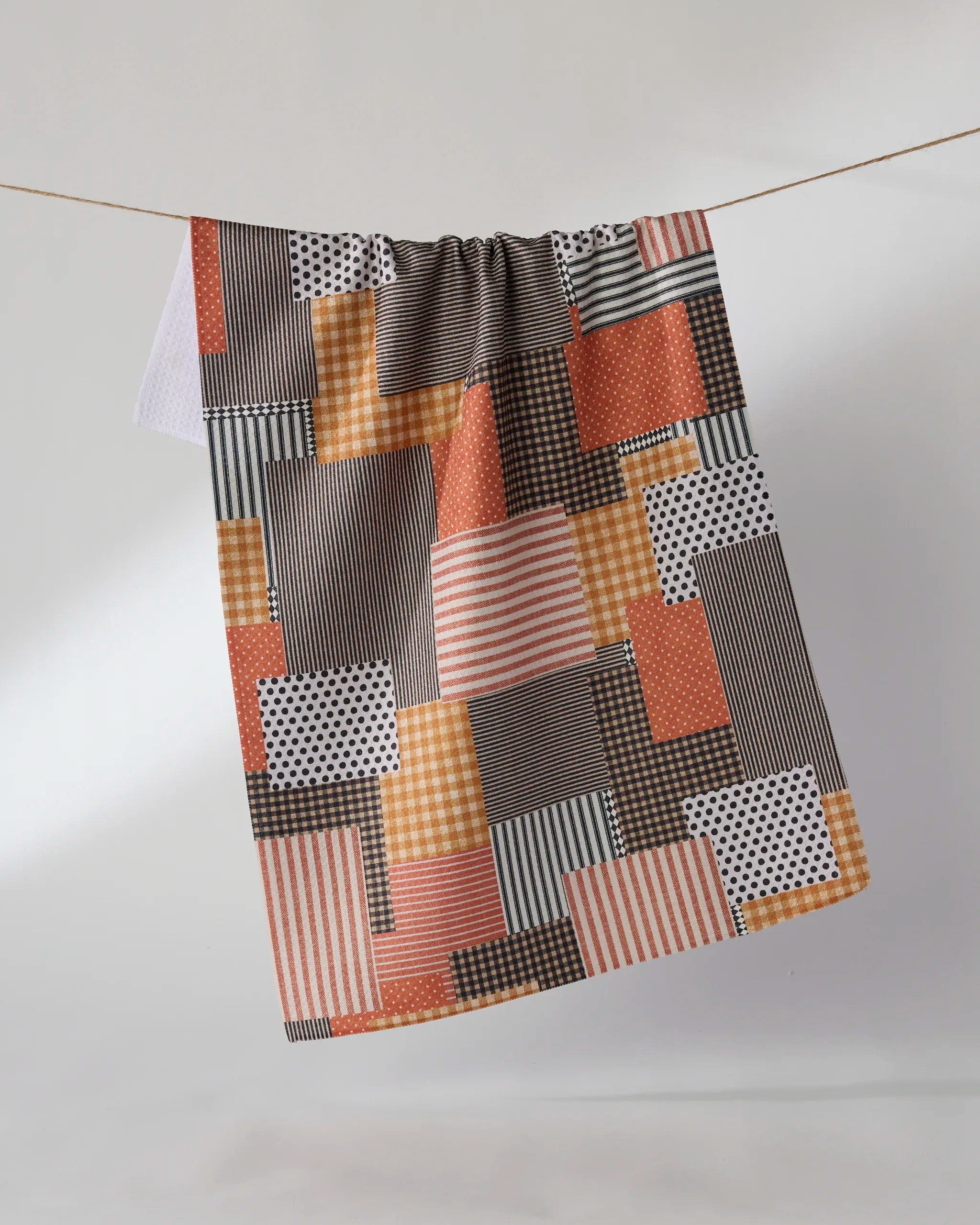 The Geometry Patch and Pumpkin tea towel, featuring vibrant orange, black, white, and brown stripes, polka dots, gingham, and solids, hangs stylishly on a clothesline. Ultra-absorbent—perfect for any kitchen.