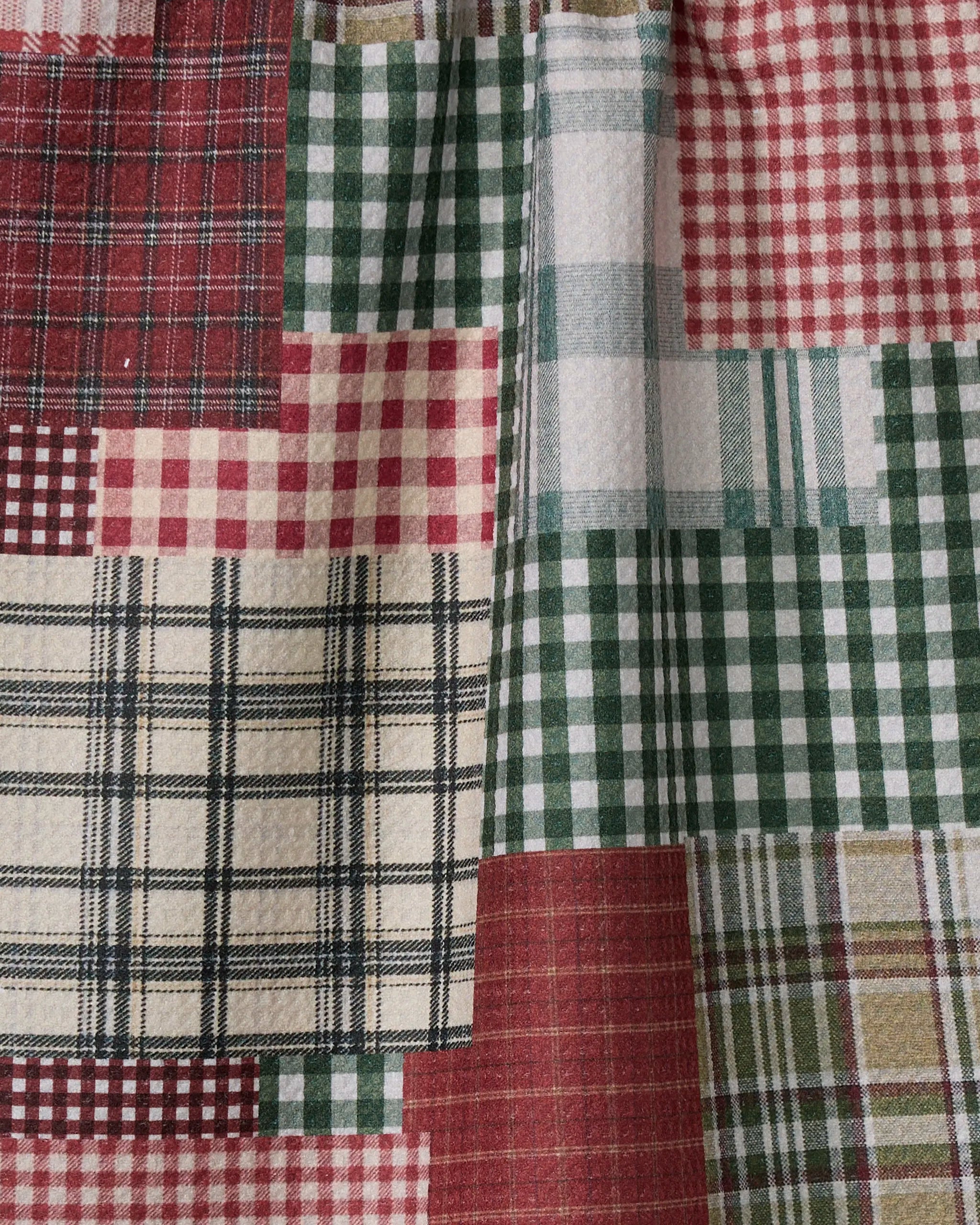 The Geometry Patchly quilt showcases red, green, cream, and beige plaid and checkered patterns in rectangular and square sections, crafted from ultra-absorbent recycled materials.