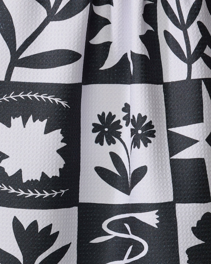 The "Patchwork" dish towel by Elana Gabrielle features a black and white grid pattern with stylized floral and leaf designs. Ultra-absorbent with visible texture, it’s both functional and beautifully crafted.