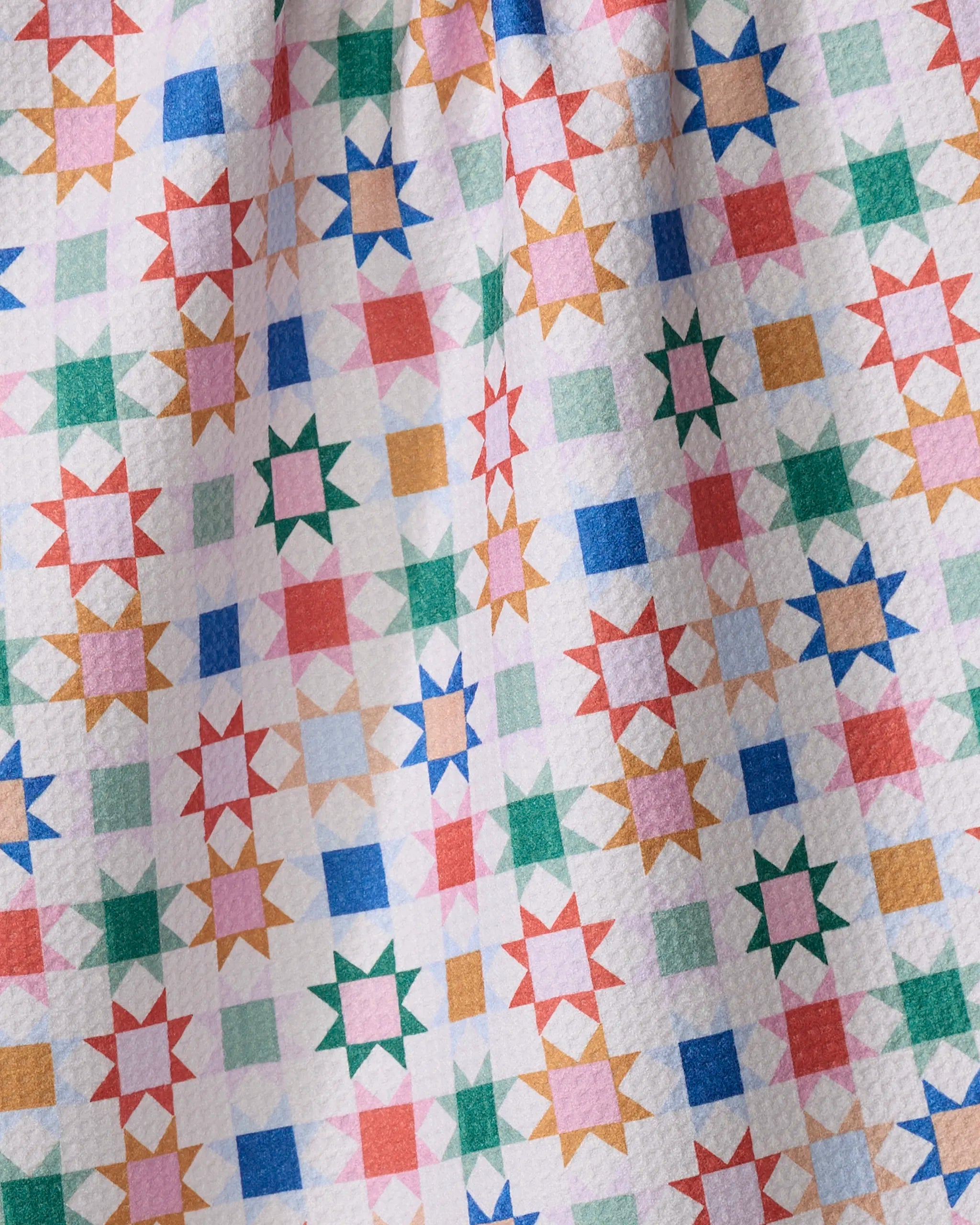 A close-up of Brittany Jepsen's Patchwork Picnic quilt, showcasing a vibrant geometric star pattern in green, blue, red, pink, and orange on white, with a textured surface like a quick-drying towel.