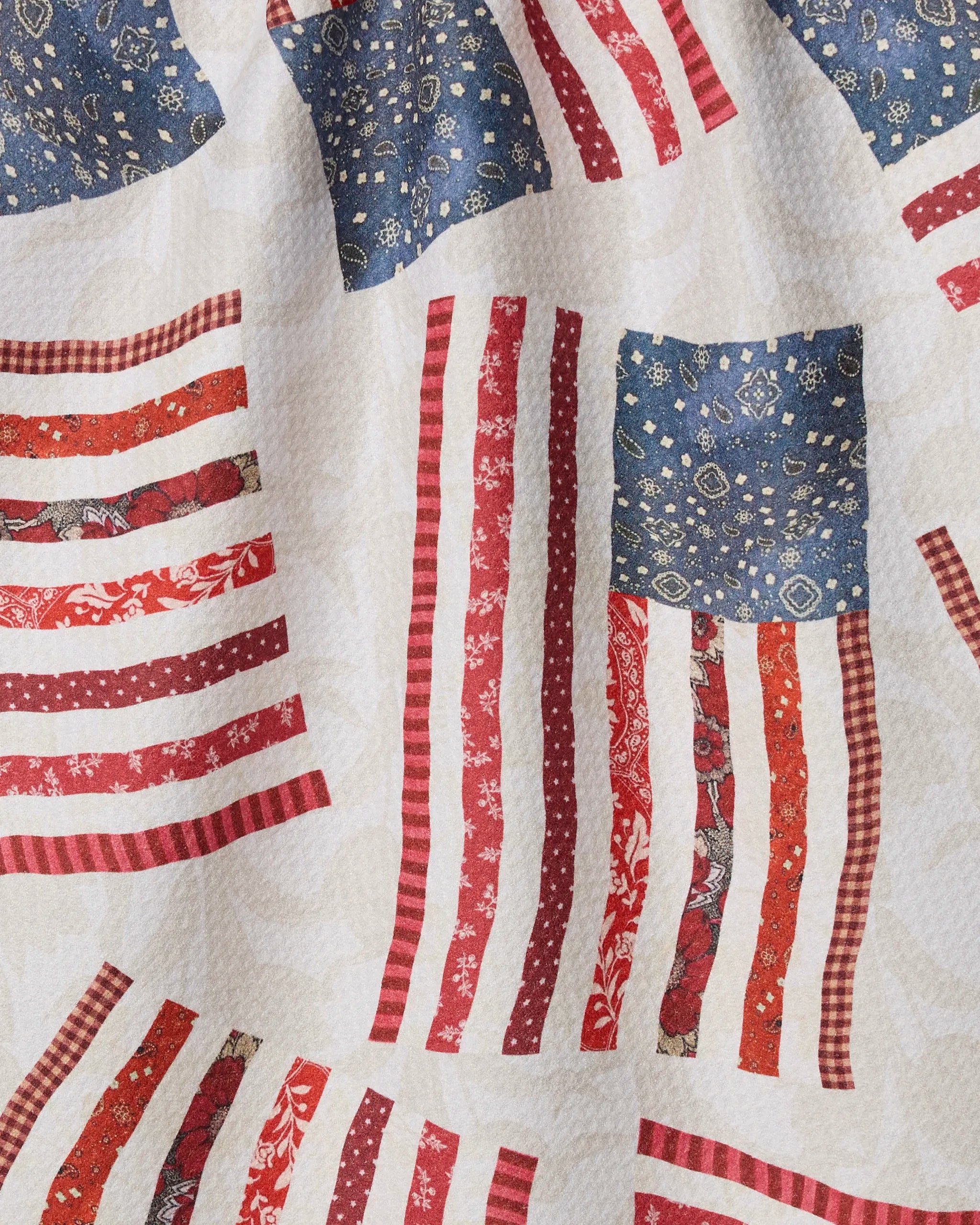 Patchwork Pride by Geometry features American flag-inspired patchwork with red and white stripes and blue fields on a cream background—ideal for an eco-friendly kitchen or tea towel.