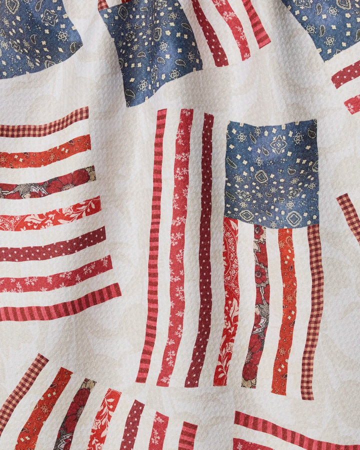 Patchwork Pride by Geometry features American flag-inspired patchwork with red and white stripes and blue fields on a cream background—ideal for an eco-friendly kitchen or tea towel.
