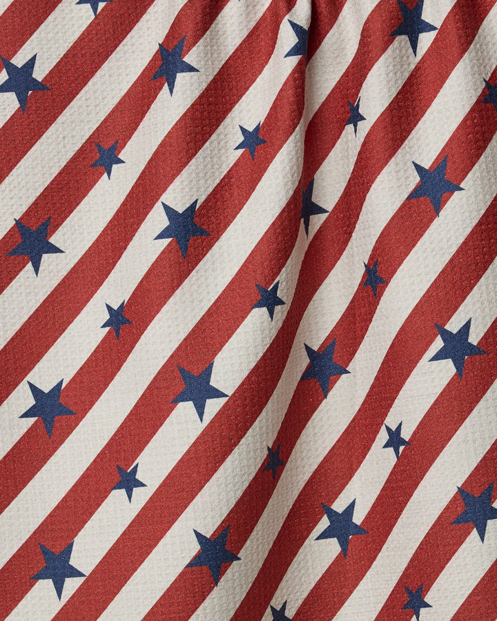 A close-up of the Geometry Patriotic Stripe kitchen towel, featuring diagonal red and white stripes with blue stars in an American flag pattern. The eco-friendly fabric, made from recycled materials, has a slightly wrinkled look.